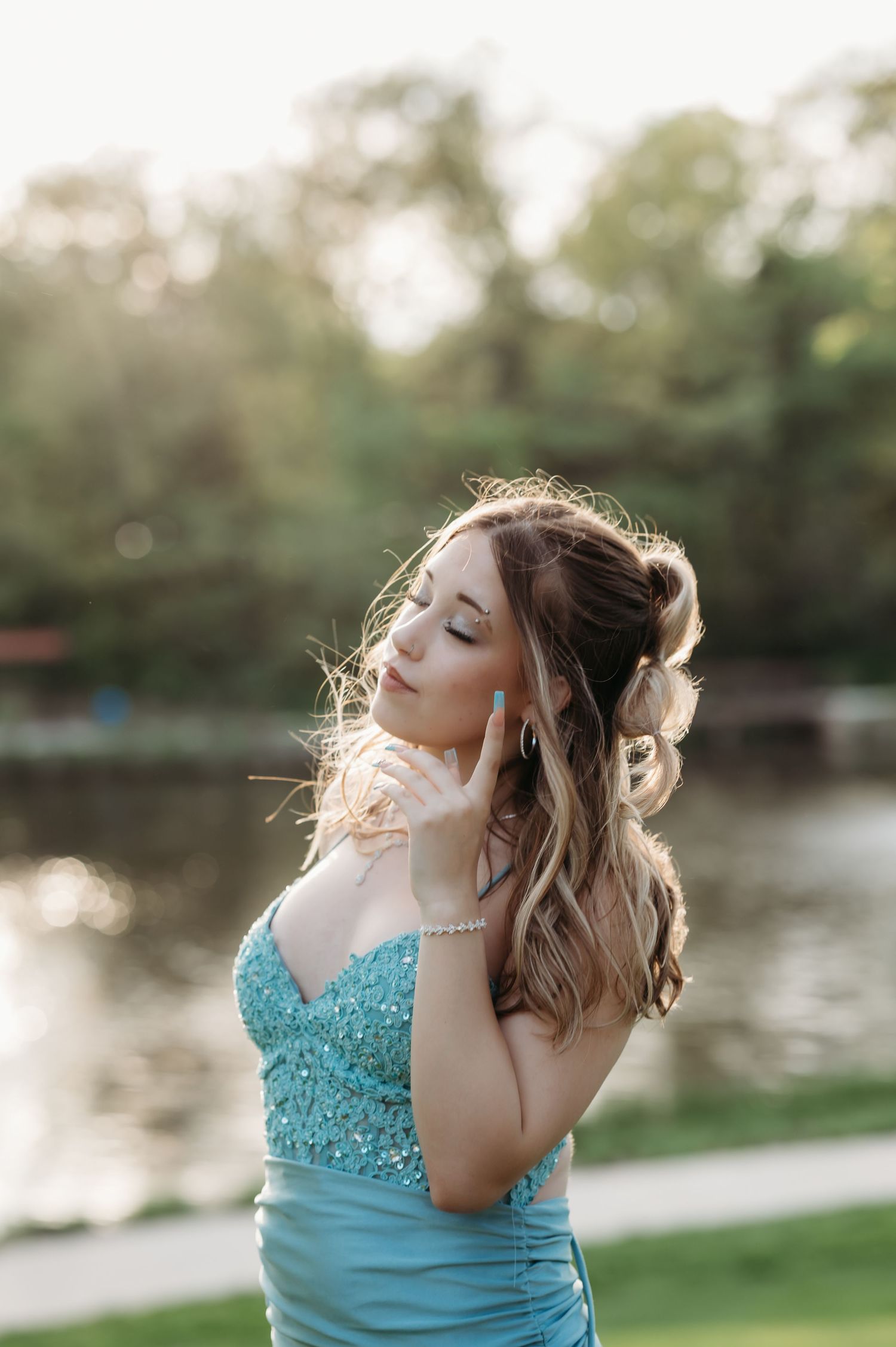 Prom client in turquoise gown poses dramatically by lake at sunset.