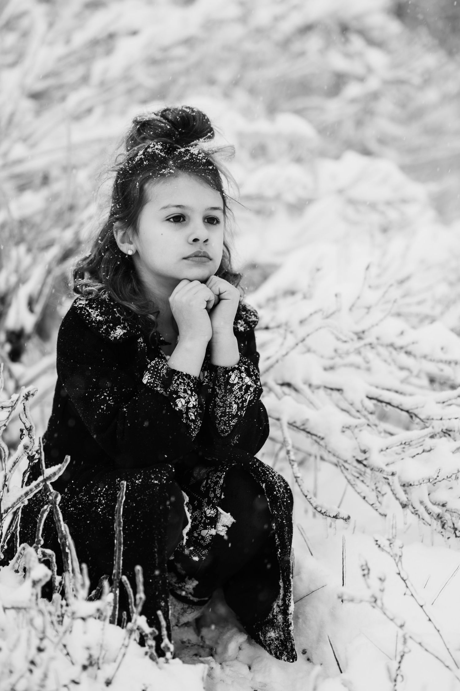 A black and white winter portrait shows someone lying in snow wearing dark clothing and looking contemplative.