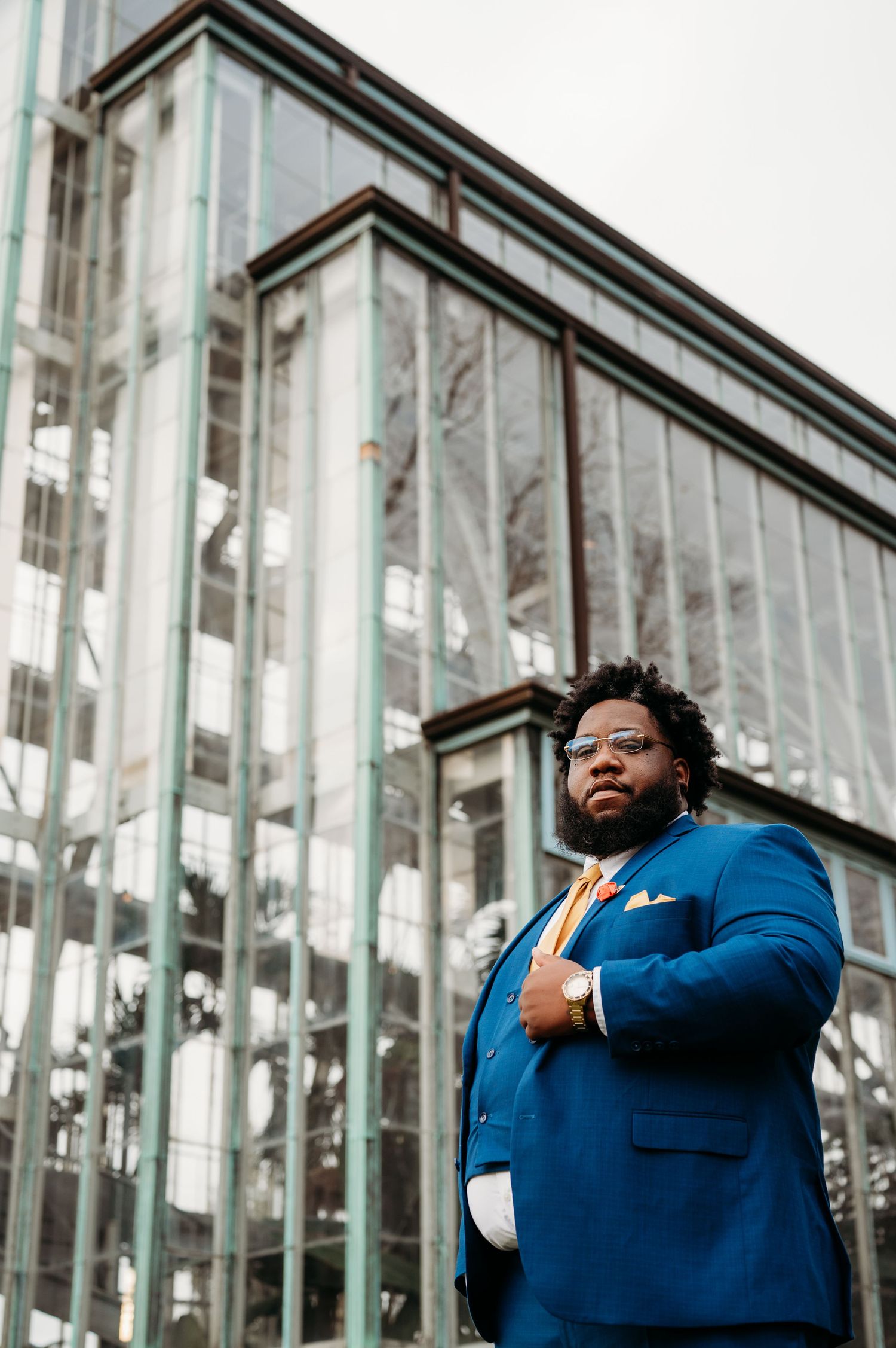 Person in blue suit poses confidently against modern glass building exterior.