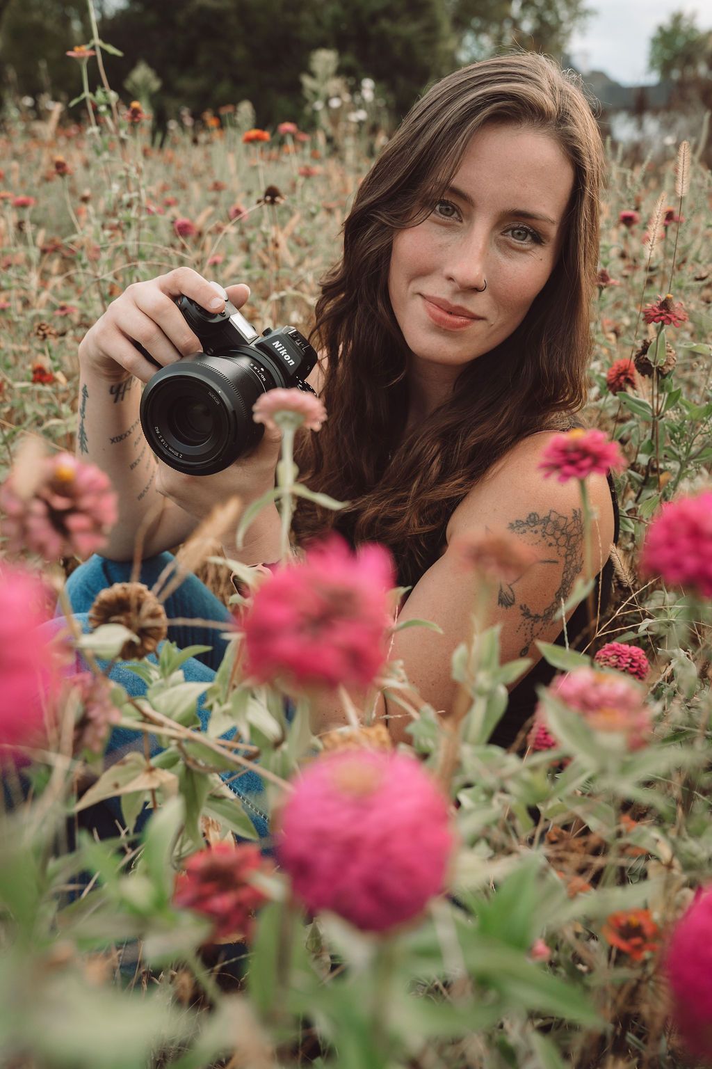 Jessica Sagerty Photography with long dark hair captures photos among vibrant pink zinnia flowers in a summer garden.