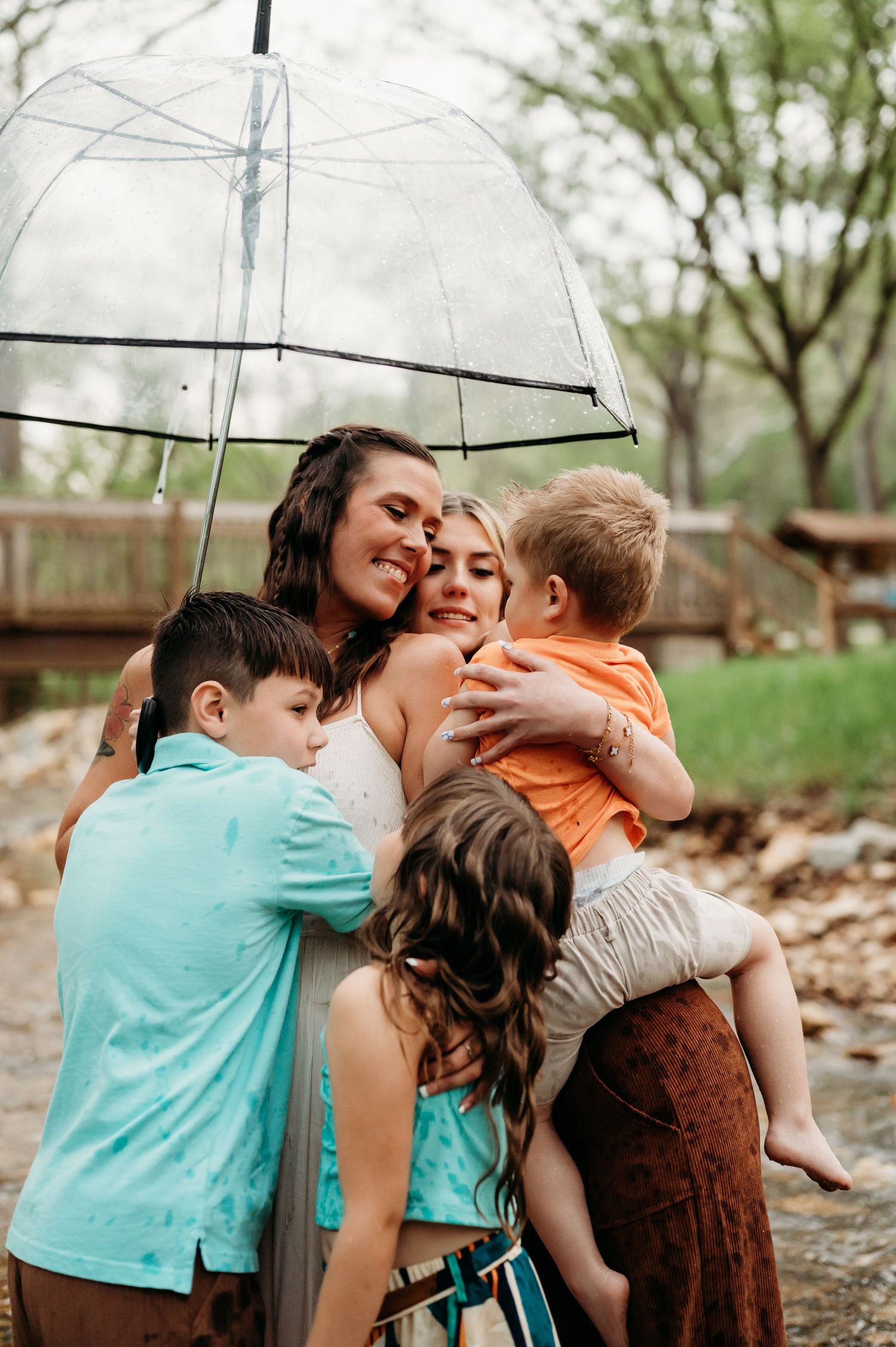 Family sharing joyful moment under clear umbrella on rainy spring day.
