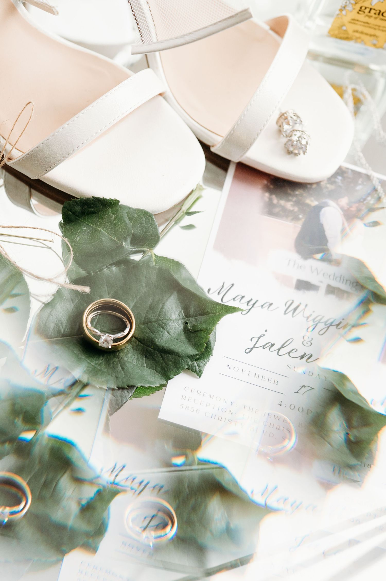 Wedding ring and invitation details with green botanical elements on white background.
