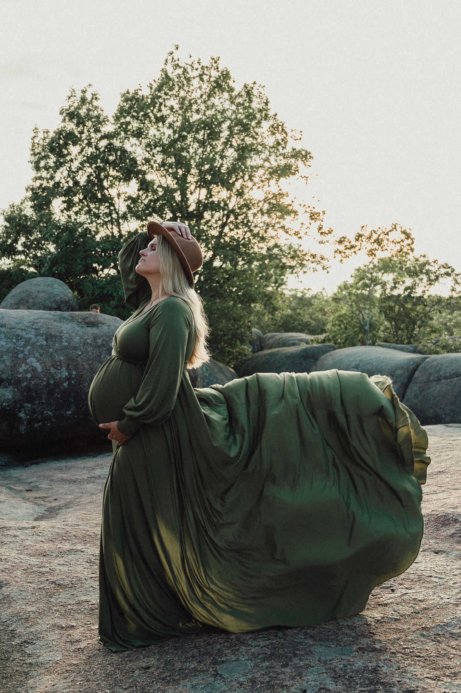Artistic maternity photo series showing flowing green dress against sunset backdrop.