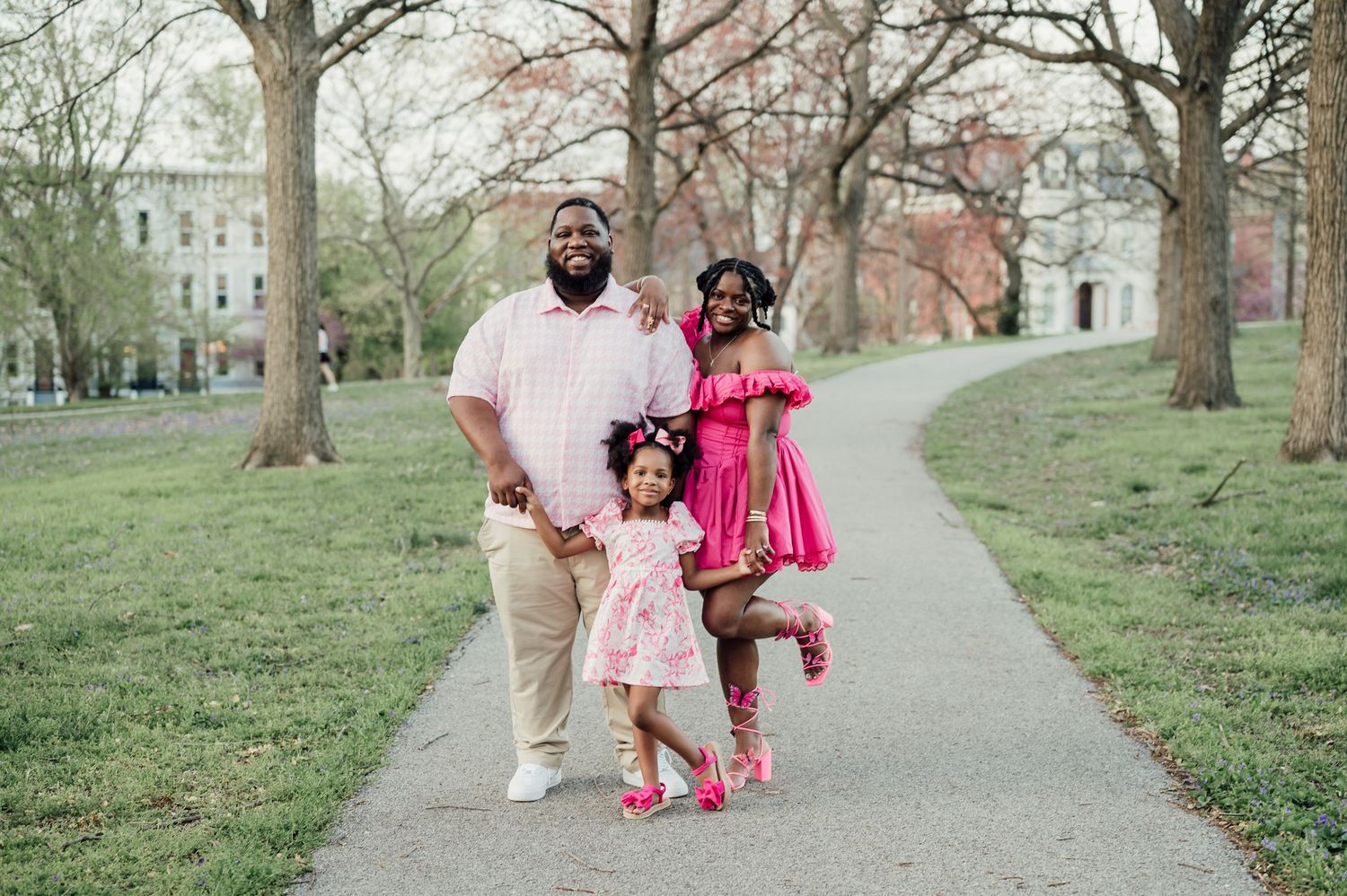 A family walking together on a tree-lined path during spring wearing coordinated pink and beige outfits.