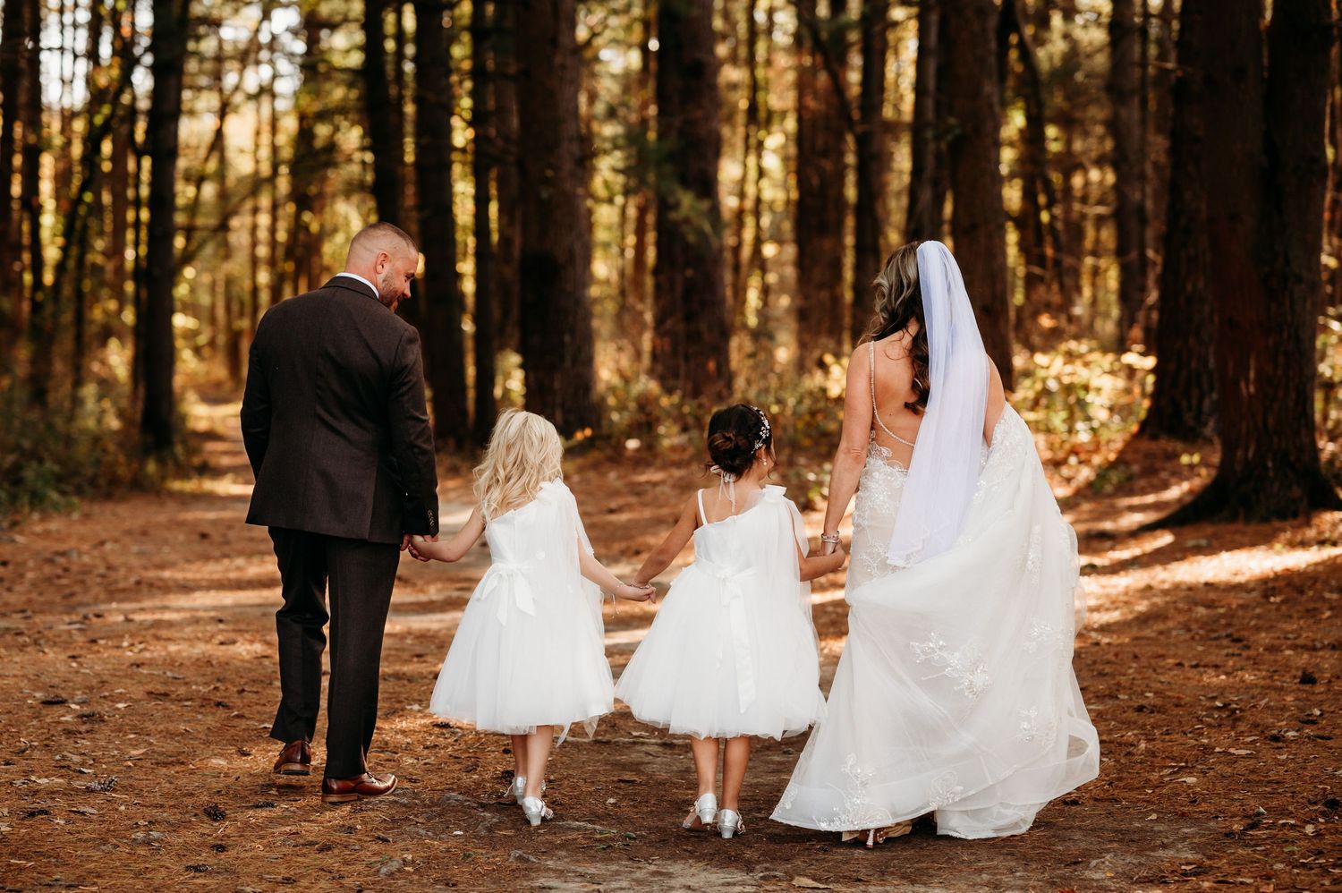 Wedding party walking through pine forest with flowing white dresses.