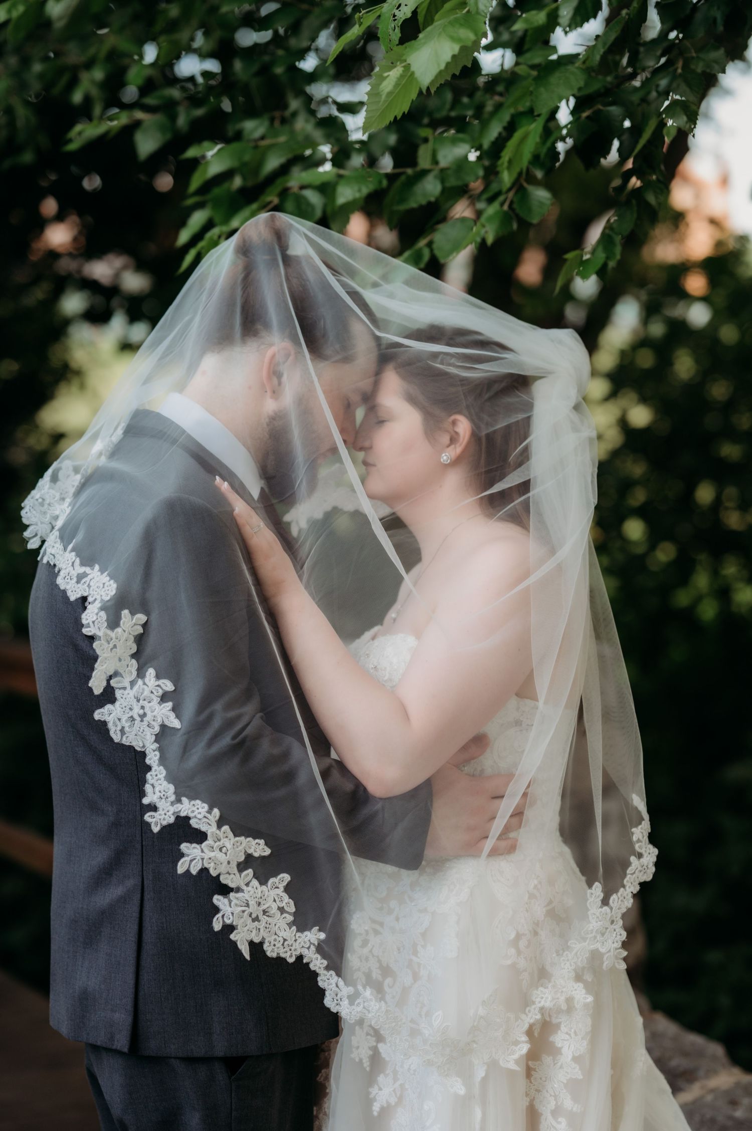 Romantic wedding portraits under a delicate lace veil in a garden setting.