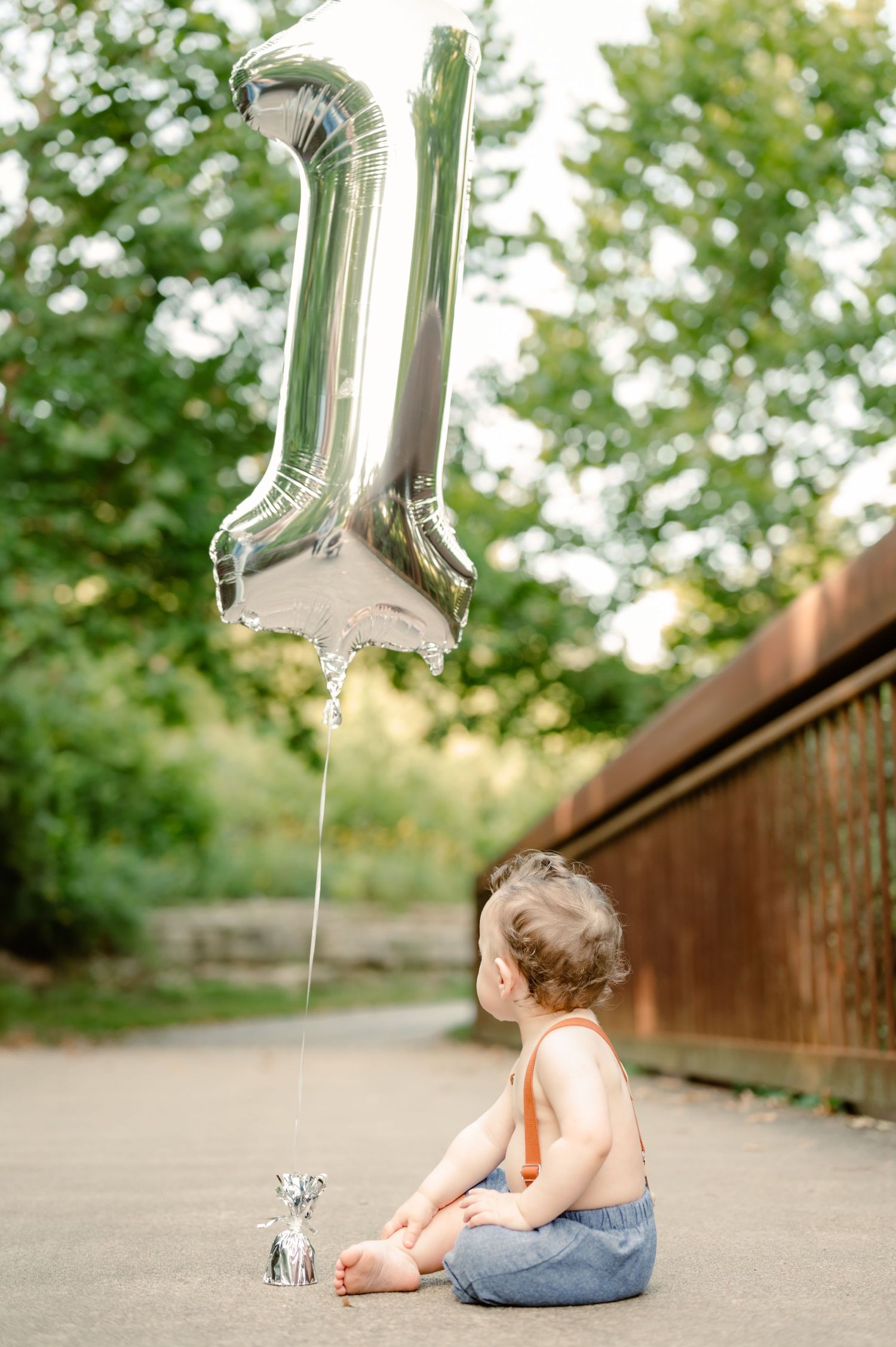 Silver number one balloon floats above child lying on path during first birthday photoshoot.