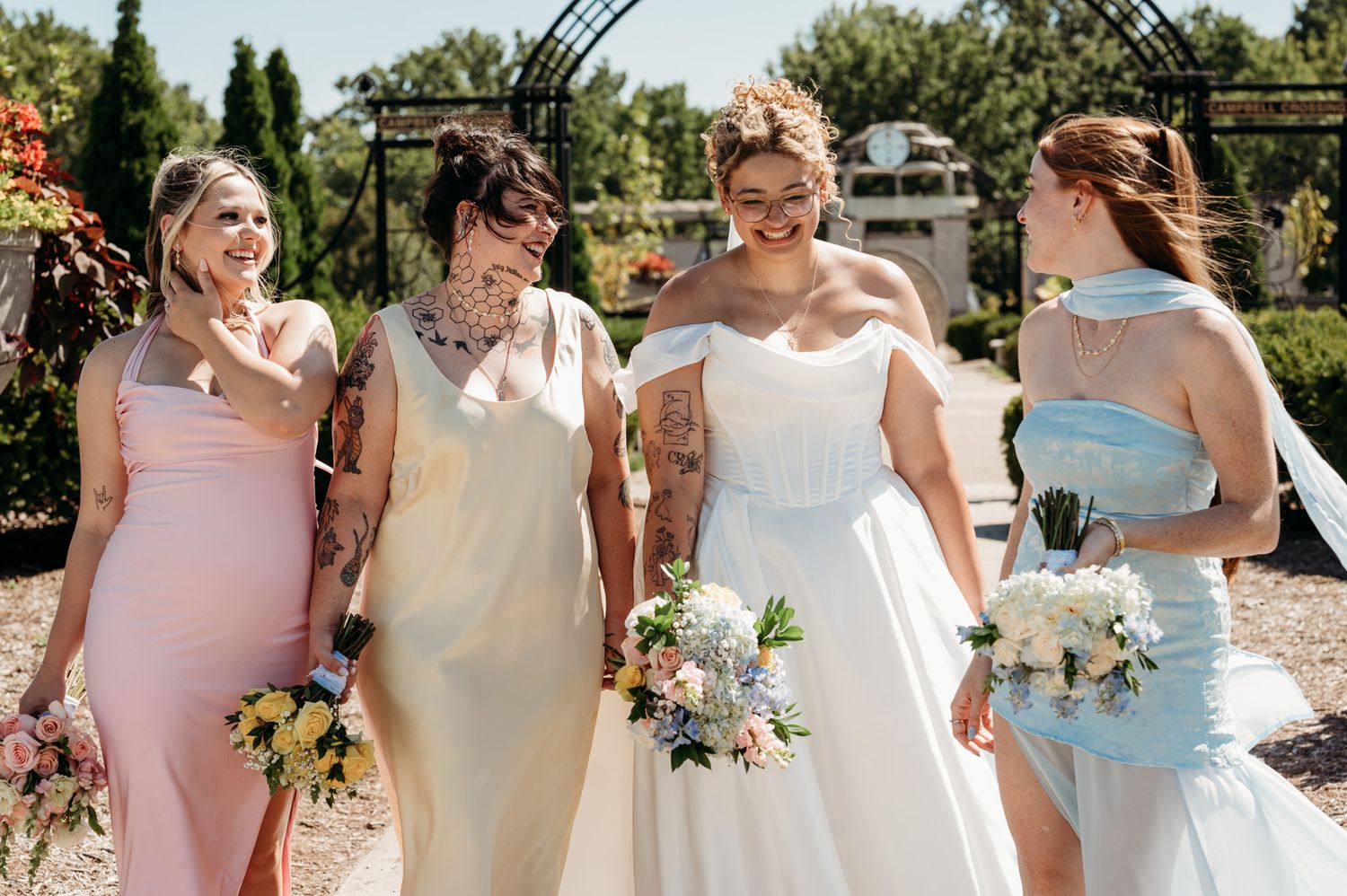 Wedding party in pastel dresses poses together in garden setting with bouquets.