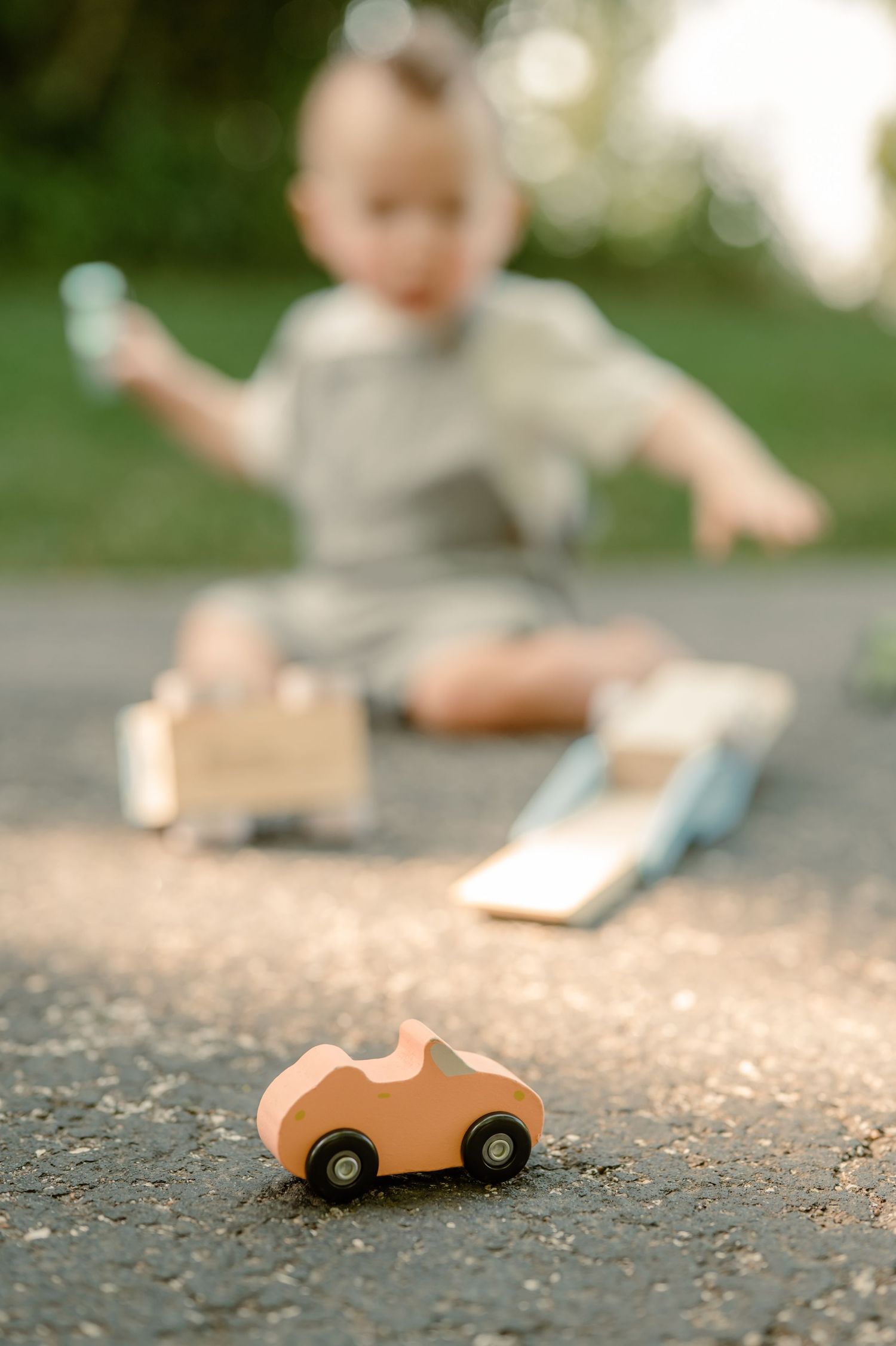 Vintage wooden toy car sits on textured ground in shallow focus photography.