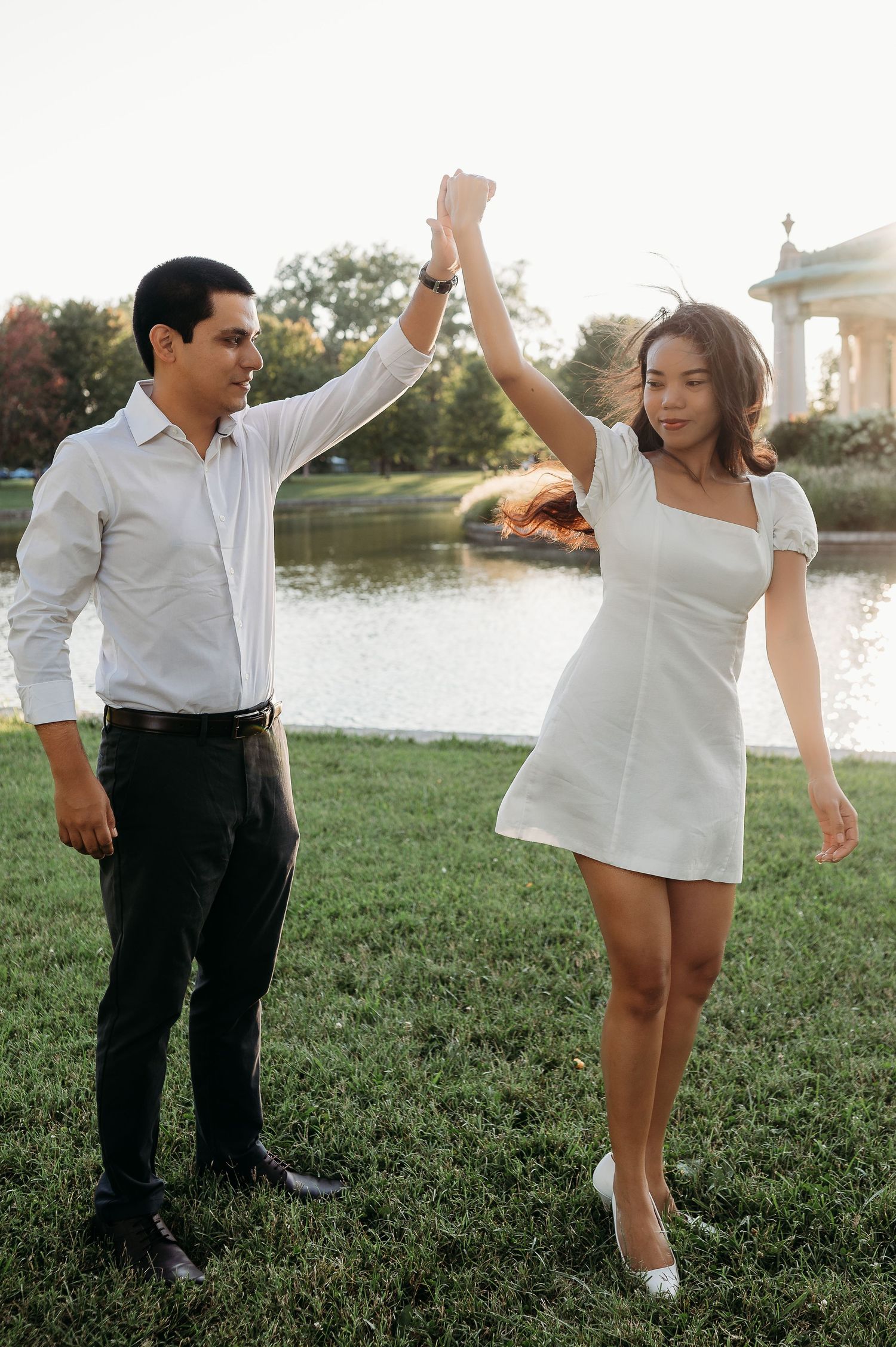 A couple dances playfully on green grass during sunset.