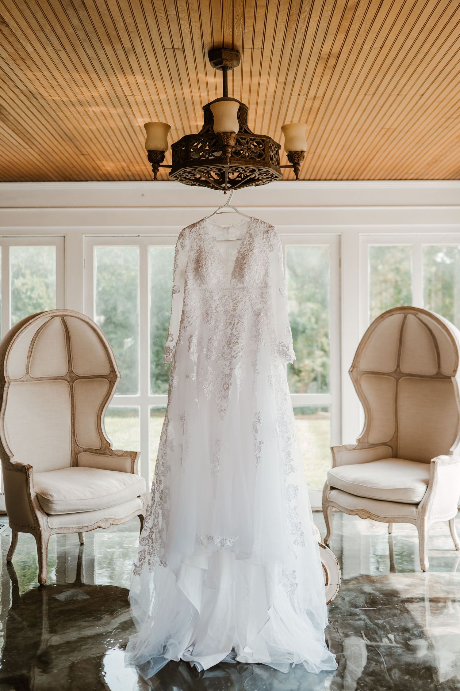 Row of elegant white wedding dresses hanging from wooden beams in a sunlit room.