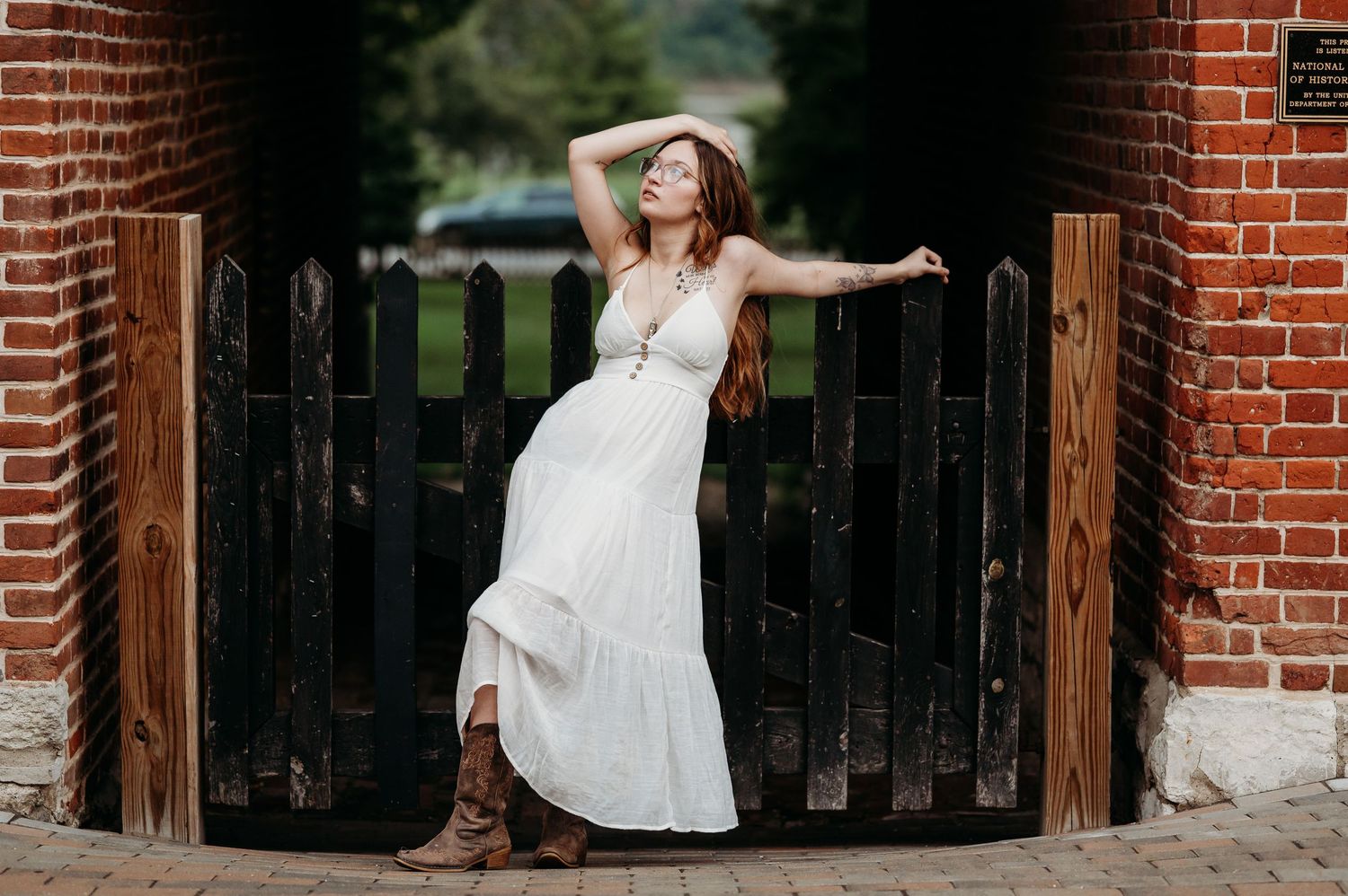 Bride in flowing white dress poses gracefully against rustic brick archways in an outdoor garden setting.