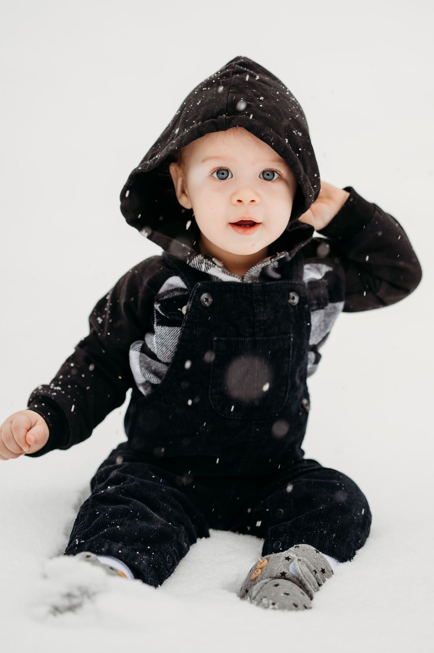 Small child wearing a black snowsuit plays in fresh white snow during winter weather.