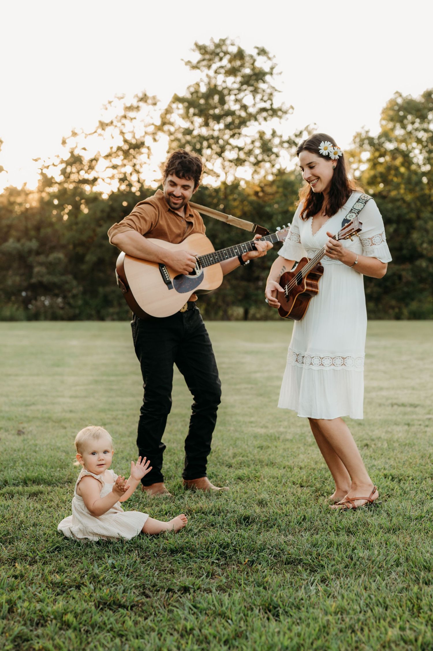 A family plays guitar and dances together on a grassy field during golden hour.