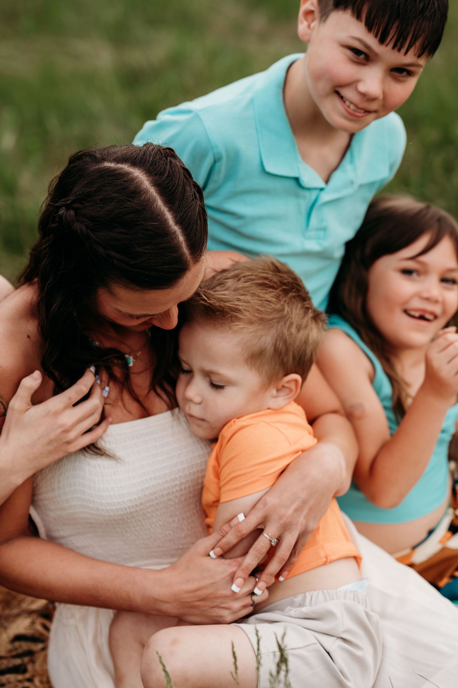 A heartwarming family moment outdoors as children and parent share loving embraces in casual summer attire.