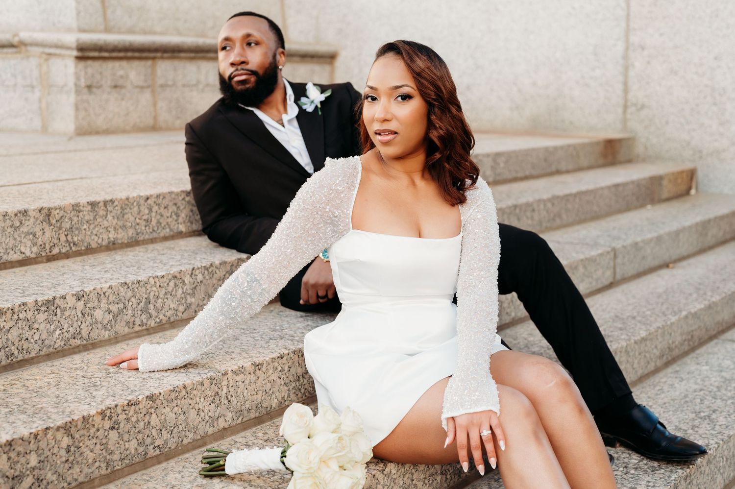 A couple in elegant wedding attire poses on stone steps during their formal photo session.