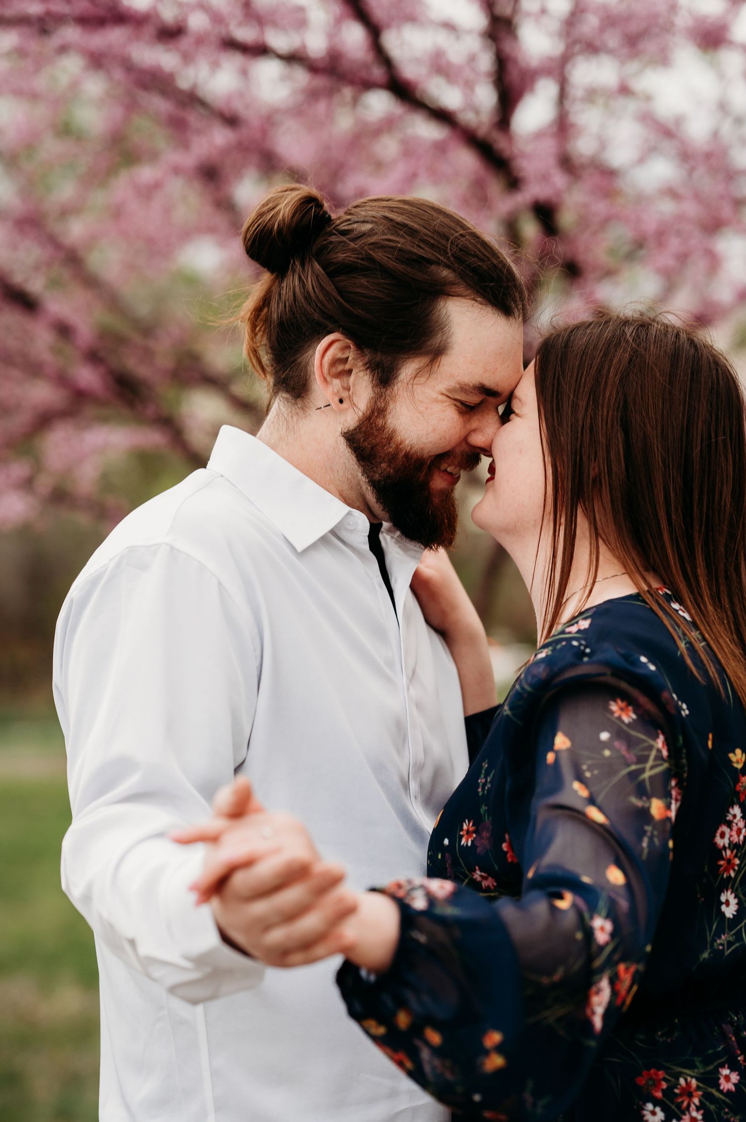 Romantic spring engagement photo under blooming cherry blossom trees.