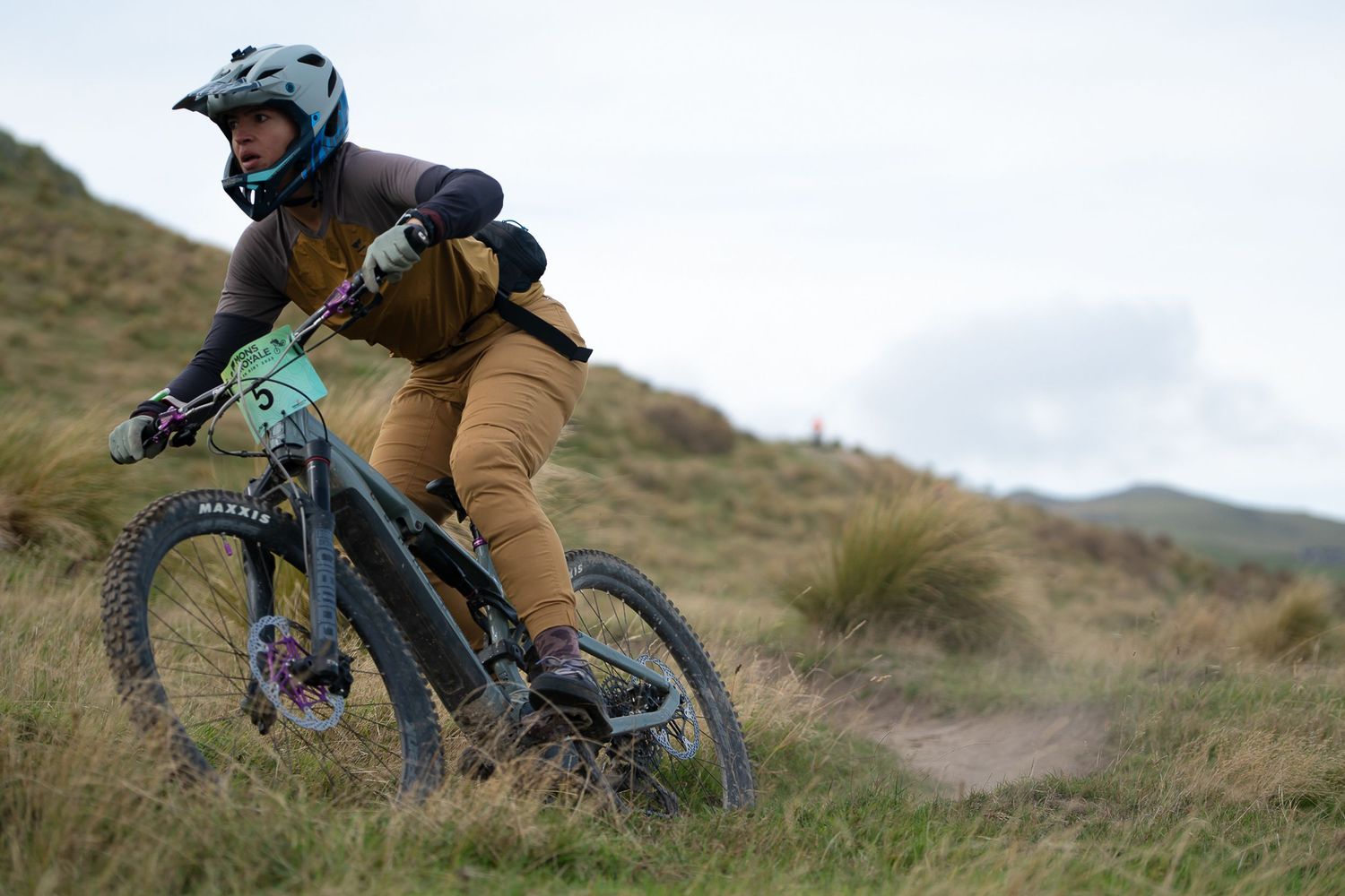 Female mountain biker descends steep terrain on a rugged trail through grassy hillsides at the Crocodile Mountain Bike Park in Halswell.