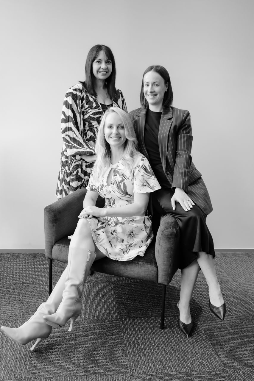 Black and white photo series showing three females sitting on a chair in a casual pose against a plain wall in Christchurch.