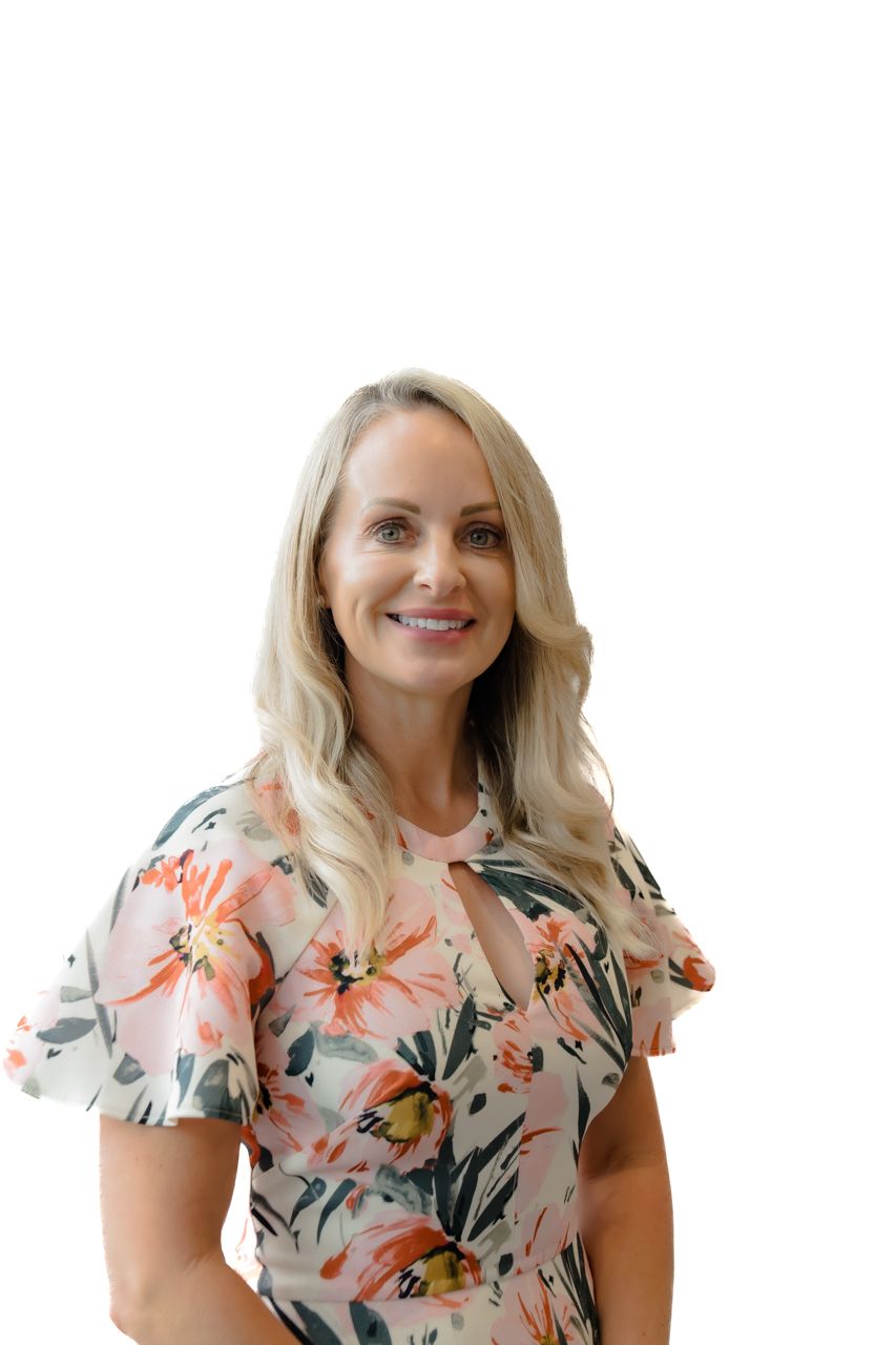 Smiling blonde woman in a floral dress posing against a white background.