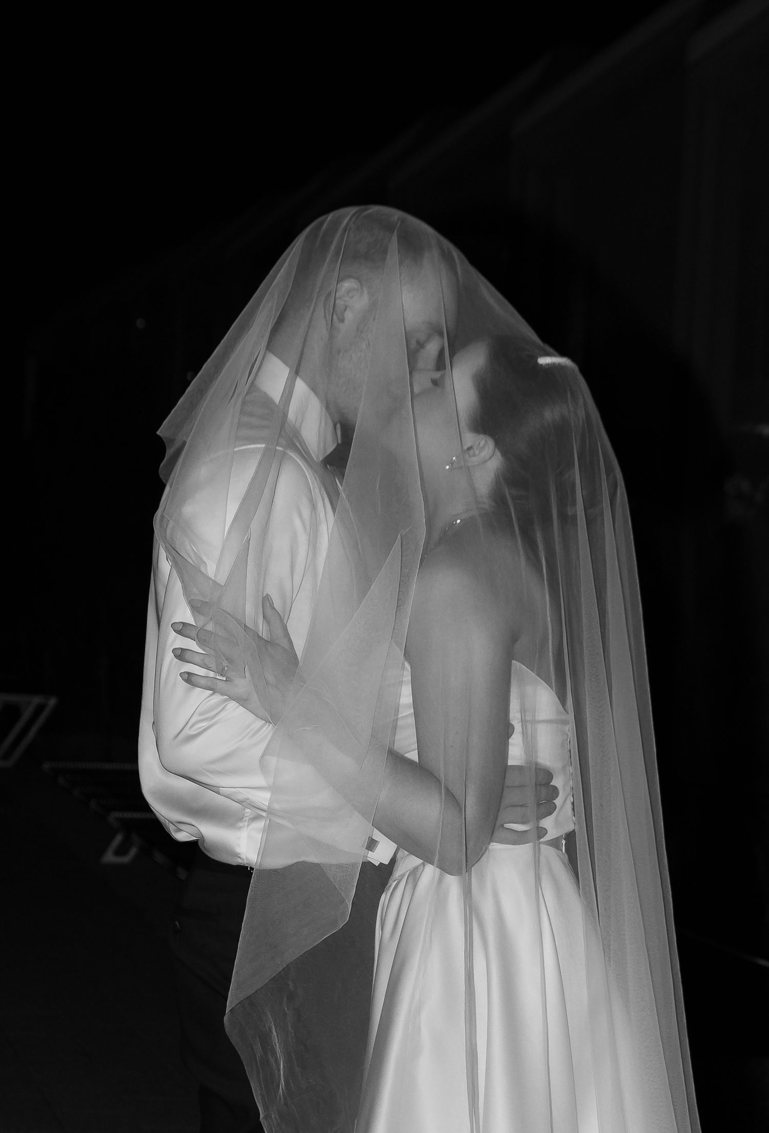 Black and white photo of a christchurch bride and groom sharing a kiss under a wedding veil.