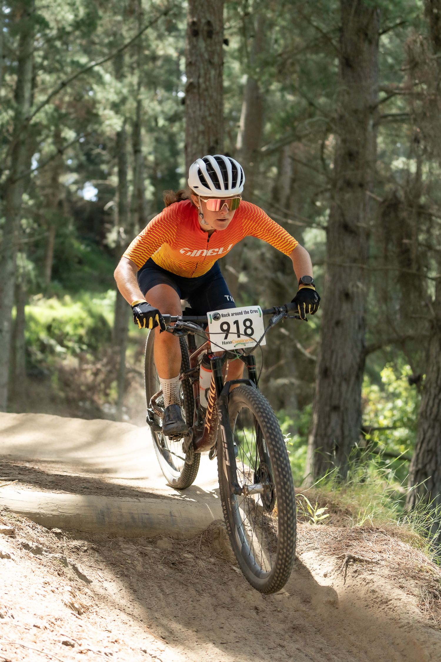 Mountain biker in orange jersey navigates a dirt trail turn through a forest of tall trees at the Halswell Crocodile Park in Christchurch.