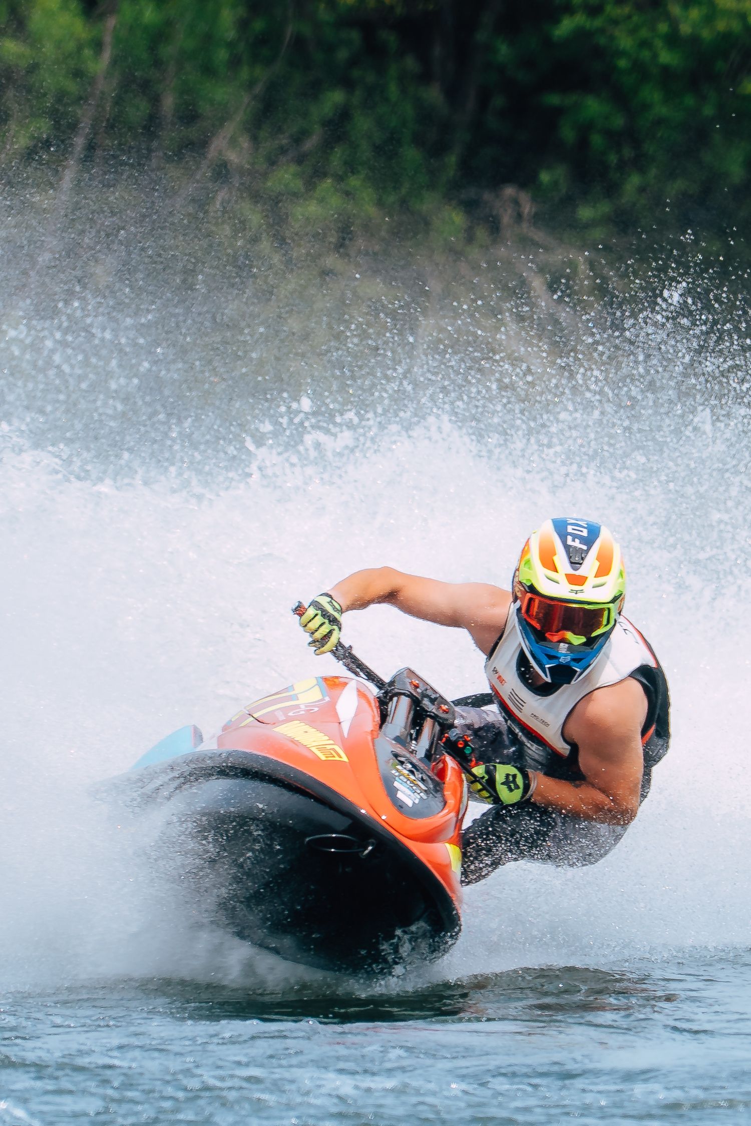 Jet ski rider on an orange jet ski performs a dramatic turn creating splash on blue water during competition in Christchurch.