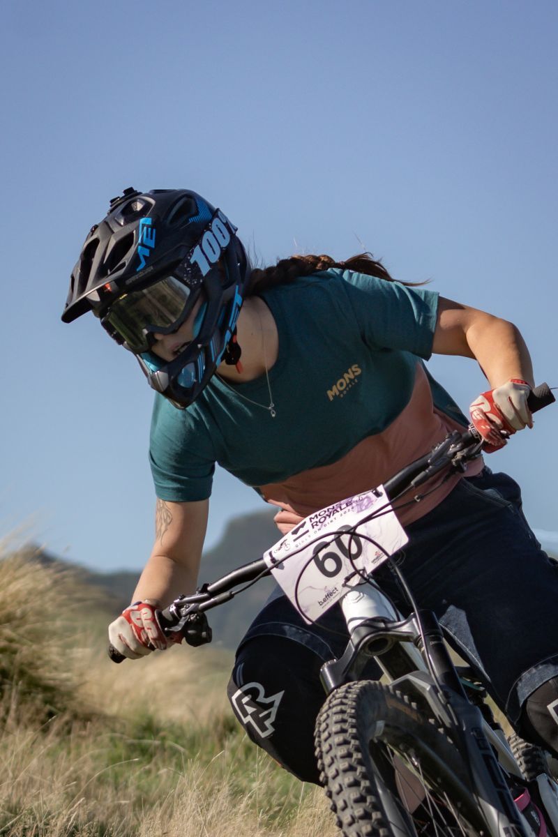 Mountain biker in green jersey riding downhill on rugged terrain against blue sky background.