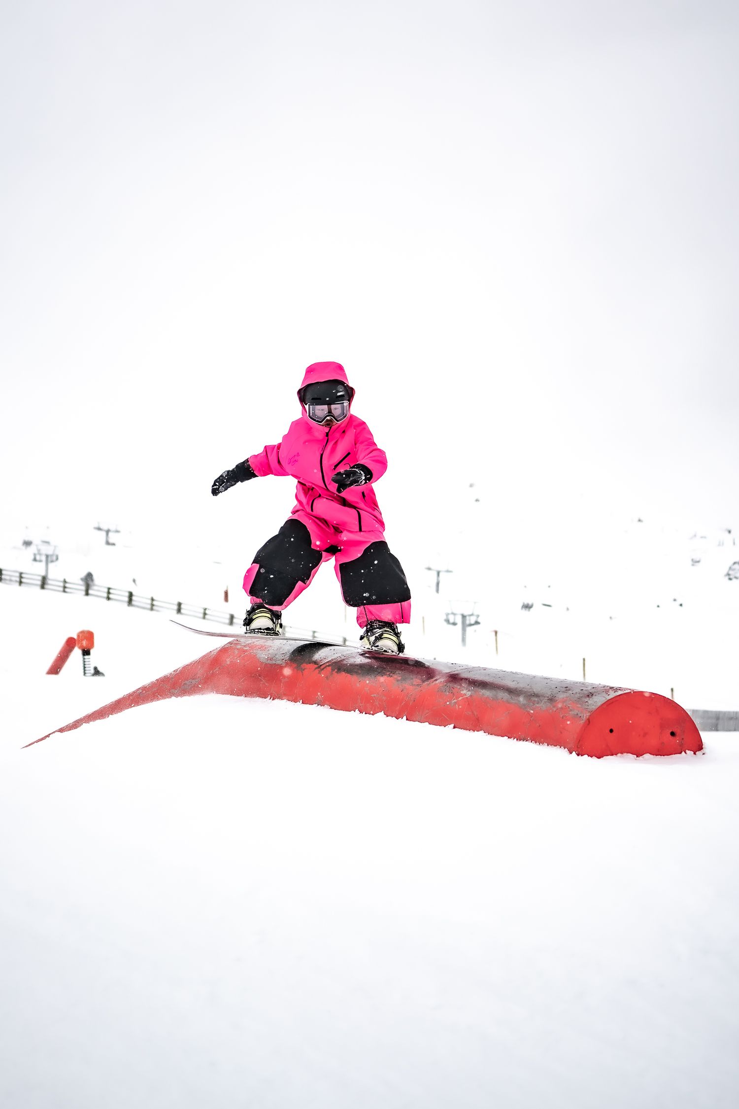 A young snowboarder in bright pink performs a trick on a snowy terrain park rail in winter conditions at Cardrona Alpine Report.