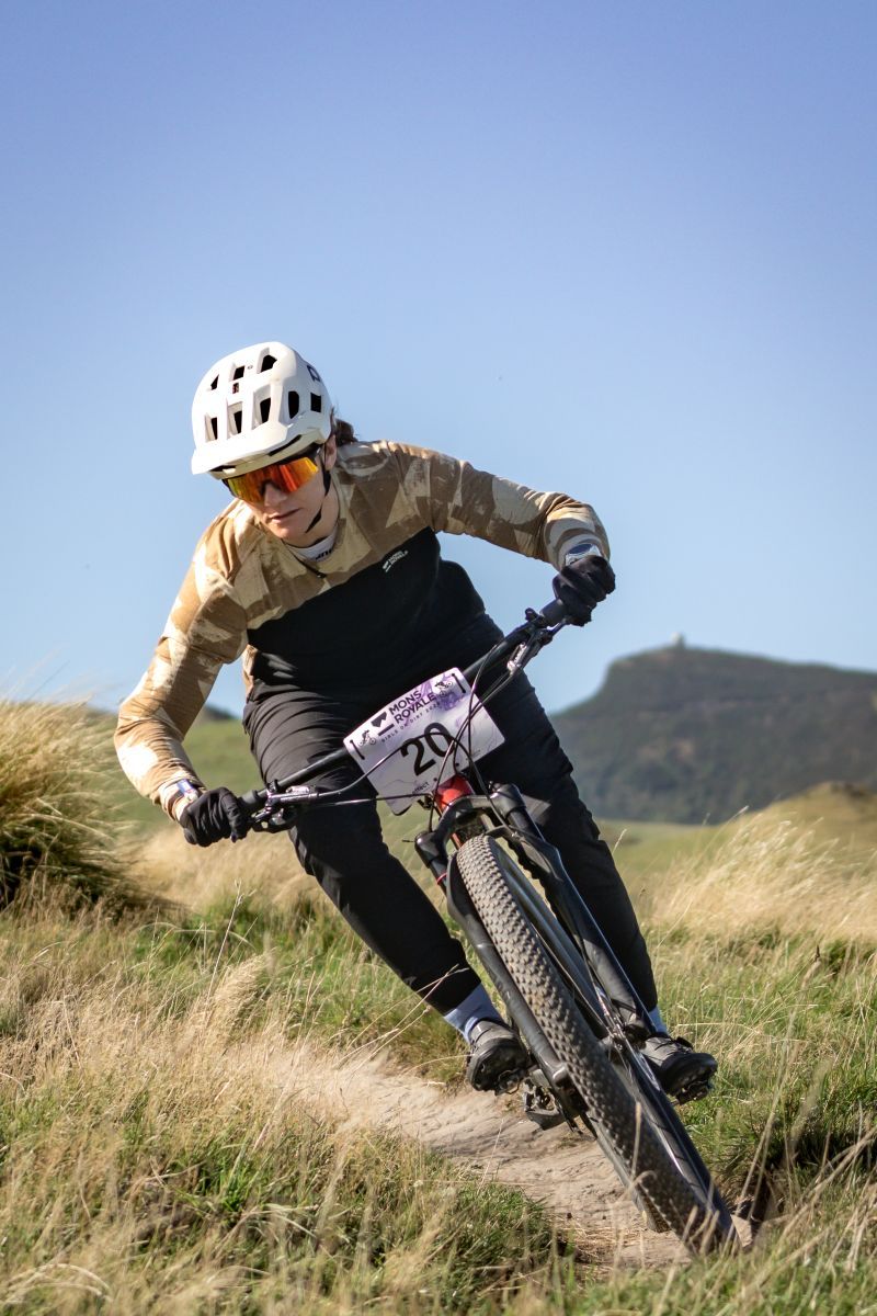 Mountain biker wearing protective gear navigates downhill trail on rugged terrain against blue sky background.