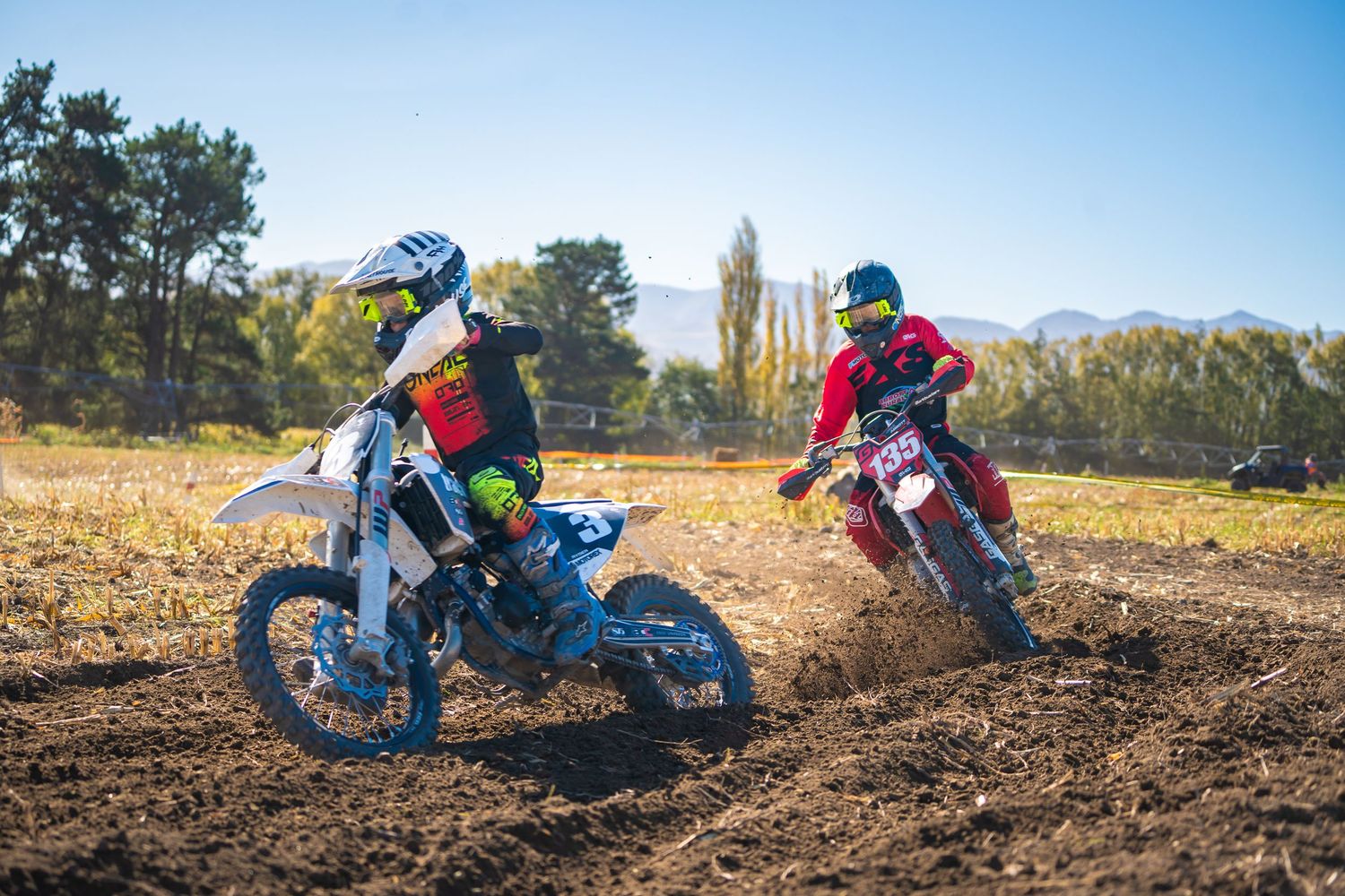 Dirt bike riders racing through a muddy track on a sunny day with trees and mountains in the background in North Canterbury.