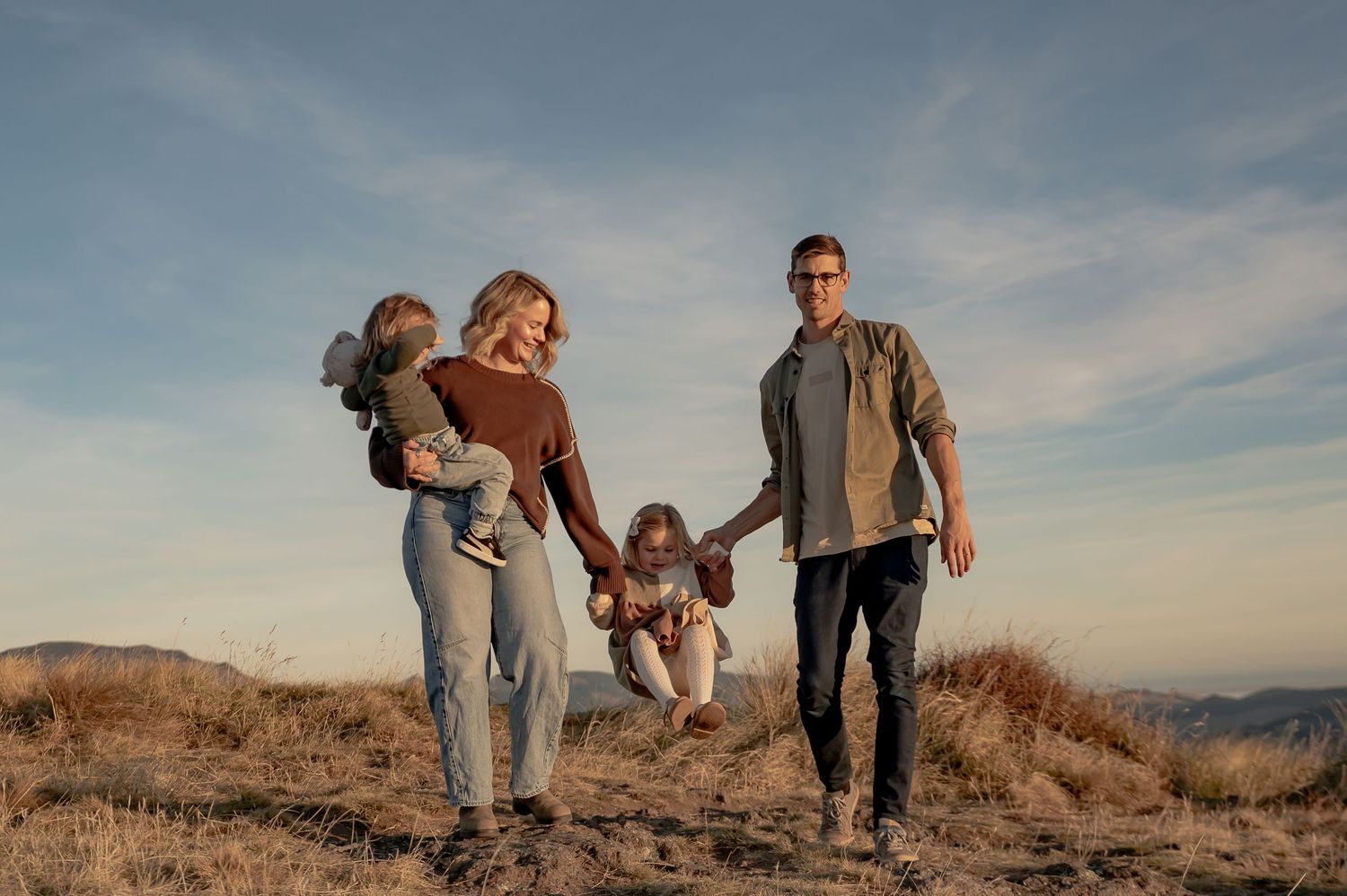 Happy family of four swinging child outdoors on a sunny day in a scenic mountain landscape.