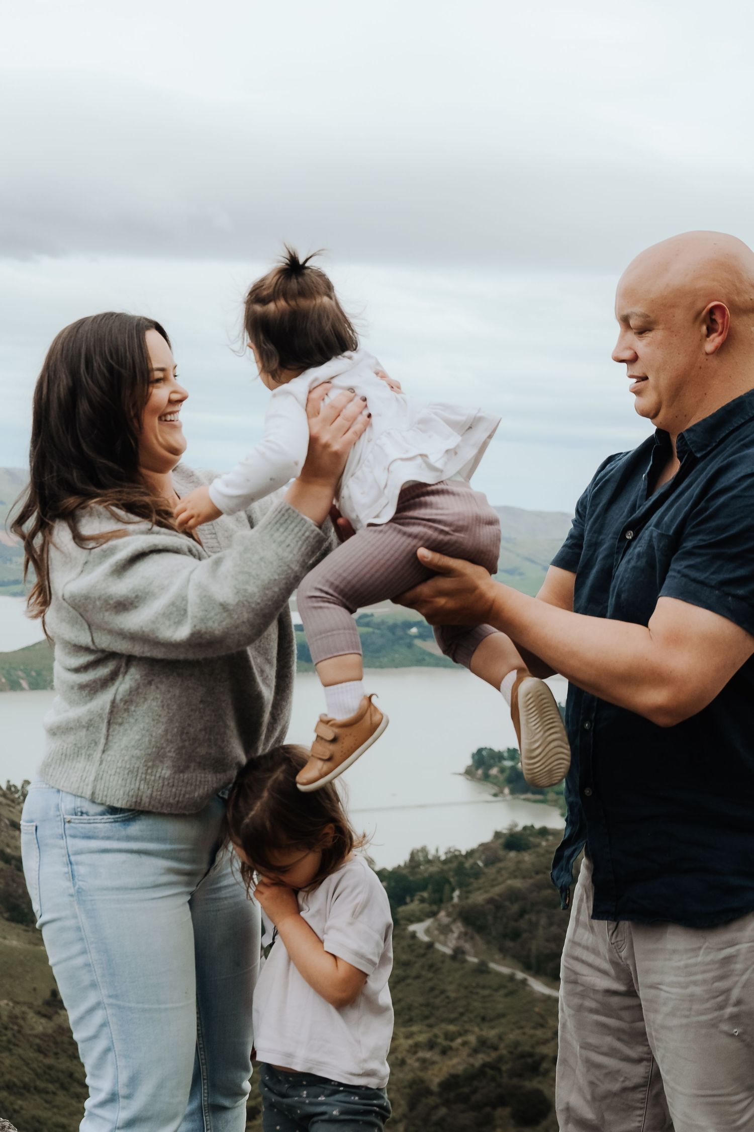 A happy family with two young children enjoys a scenic overlook with a lake and hills in the background.