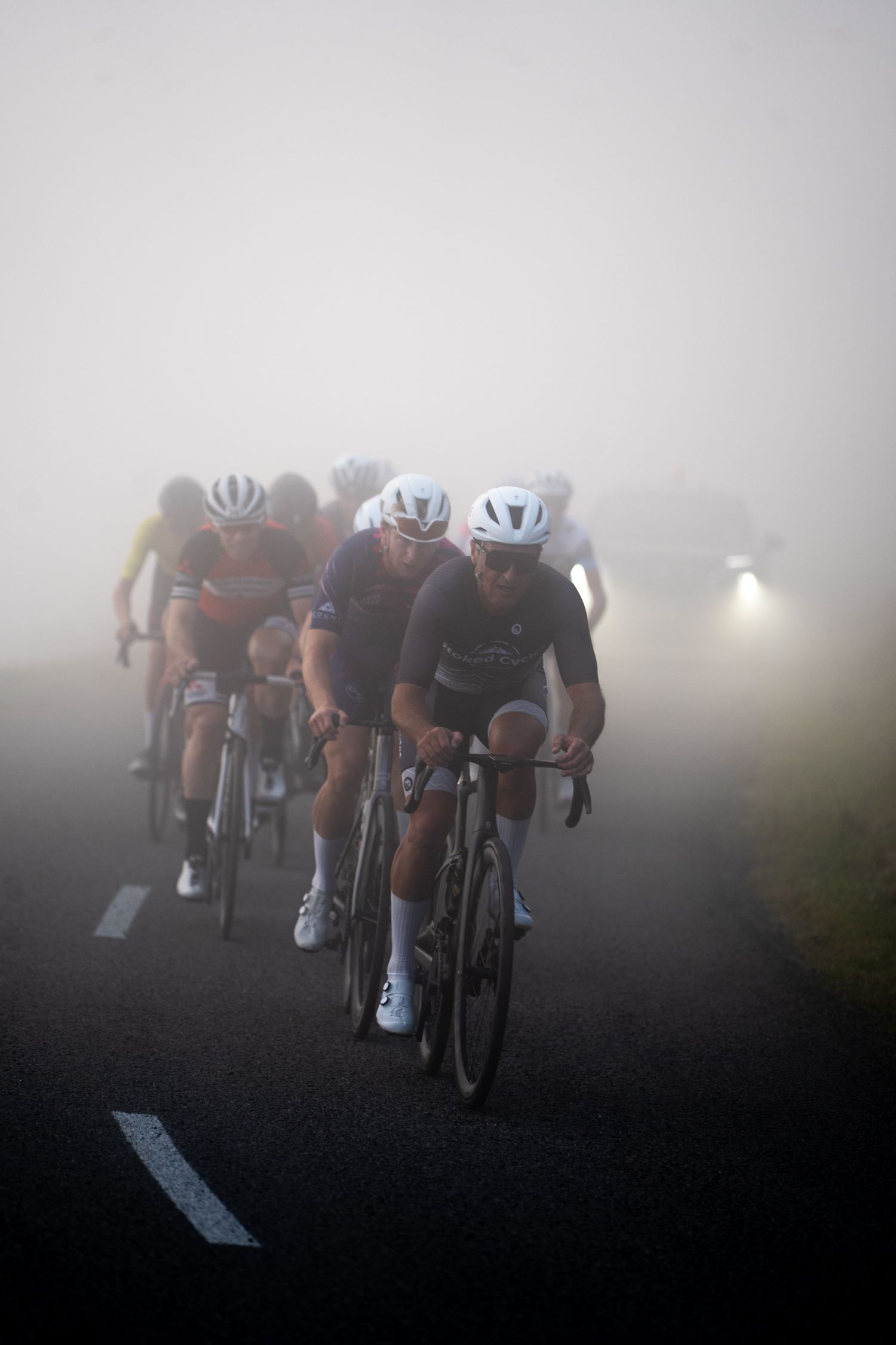 Road cyclists riding in foggy conditions along the Christchurch Port Hills during the 2025 Le Race.