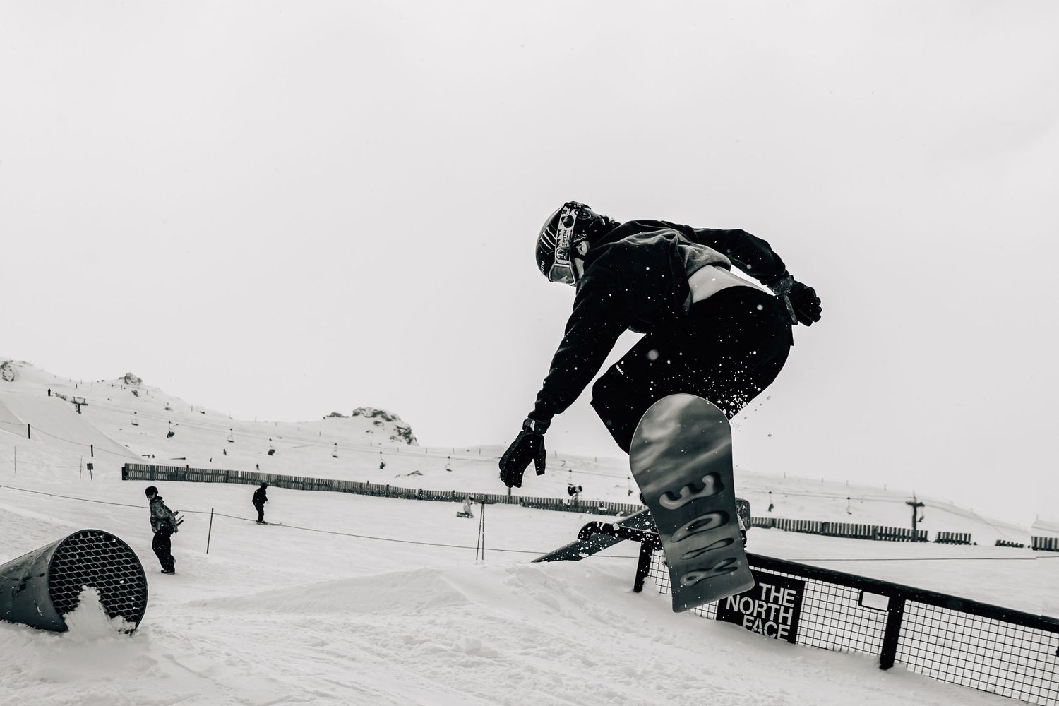 A female snowboarder performs a trick at Cardrona Alpine Report with mountains in the background.