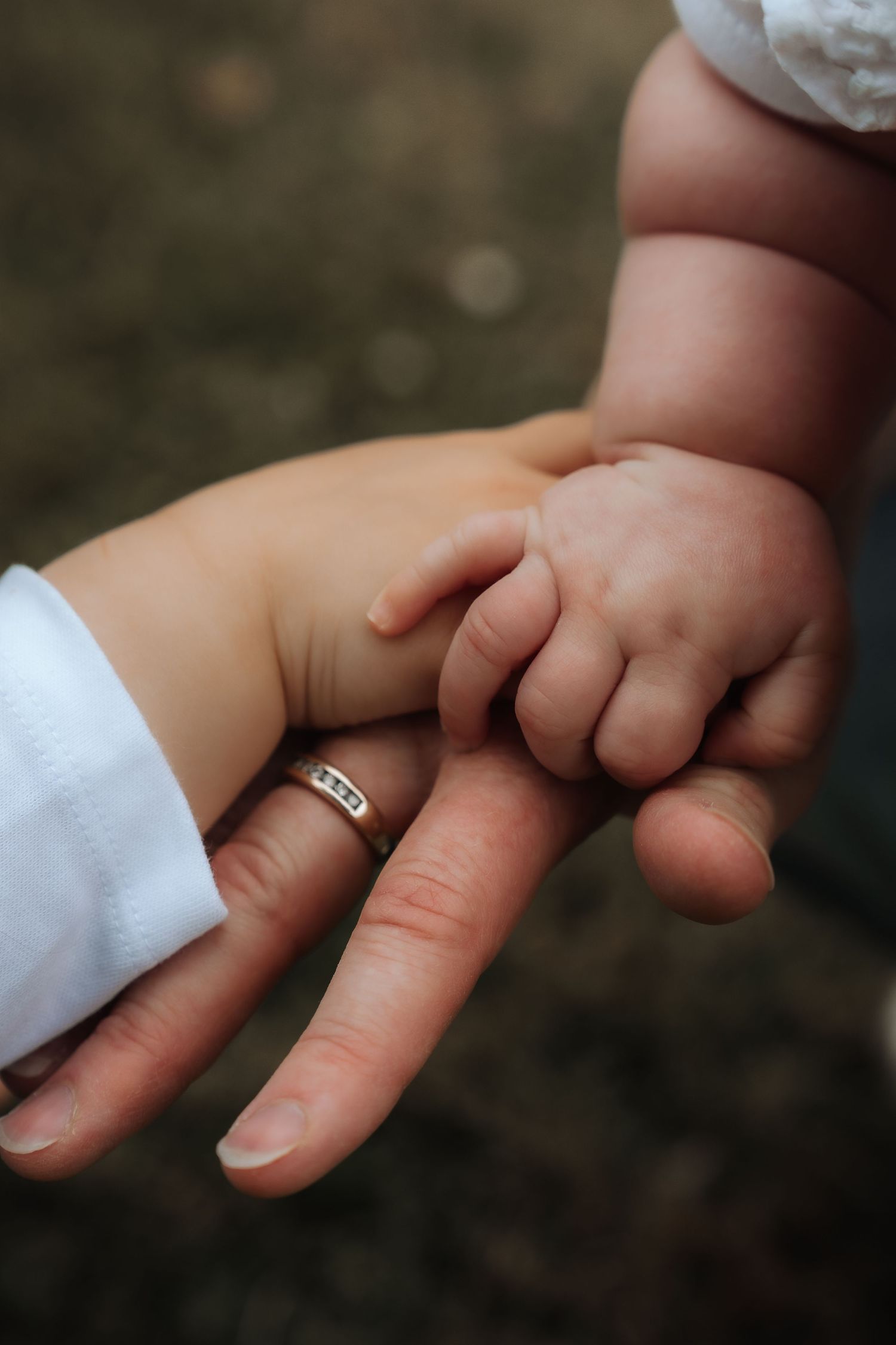 A newborn baby's tiny hand grasping an adult's finger wearing a wedding ring, symbolizing new parenthood.