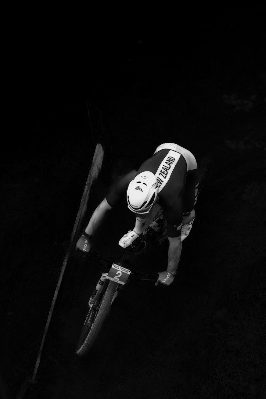Black and white aerial view of a New Zealand cyclist racing on a mountain bike track.