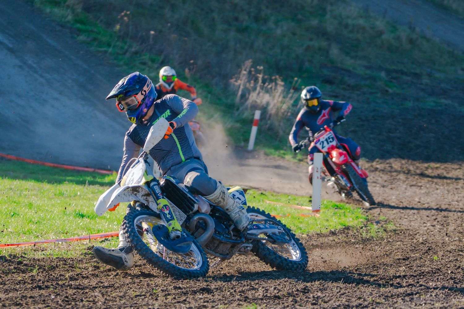 Motocross riders lean into a dirt track turn showing advanced cornering technique during a race at the Michael Godfrey Memorial Race 2025.
