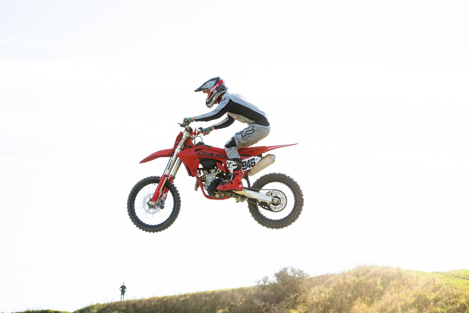 A dirt bike rider performs a dramatic jump over a hill during an off-road motocross competition on the West Coast, South Island of NZ.