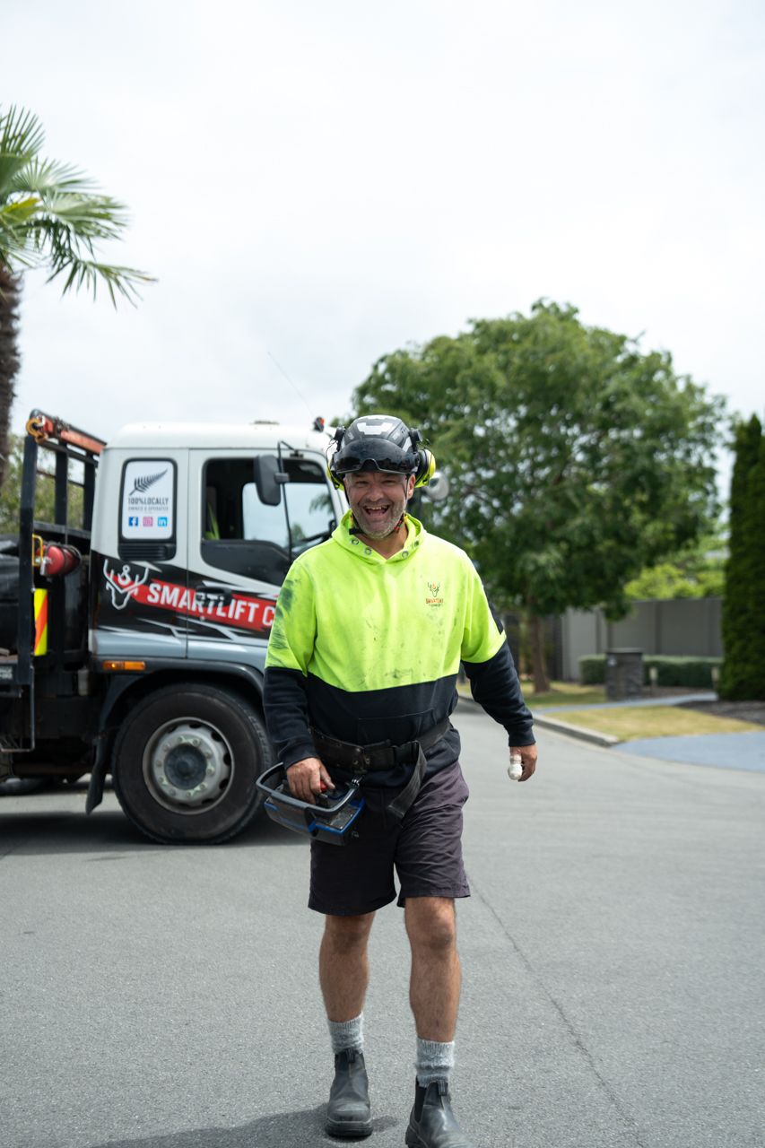 Smiling Smartlift worker in hi-vis gear holding a helmet, standing in front of a Smartlift truck outdoors.