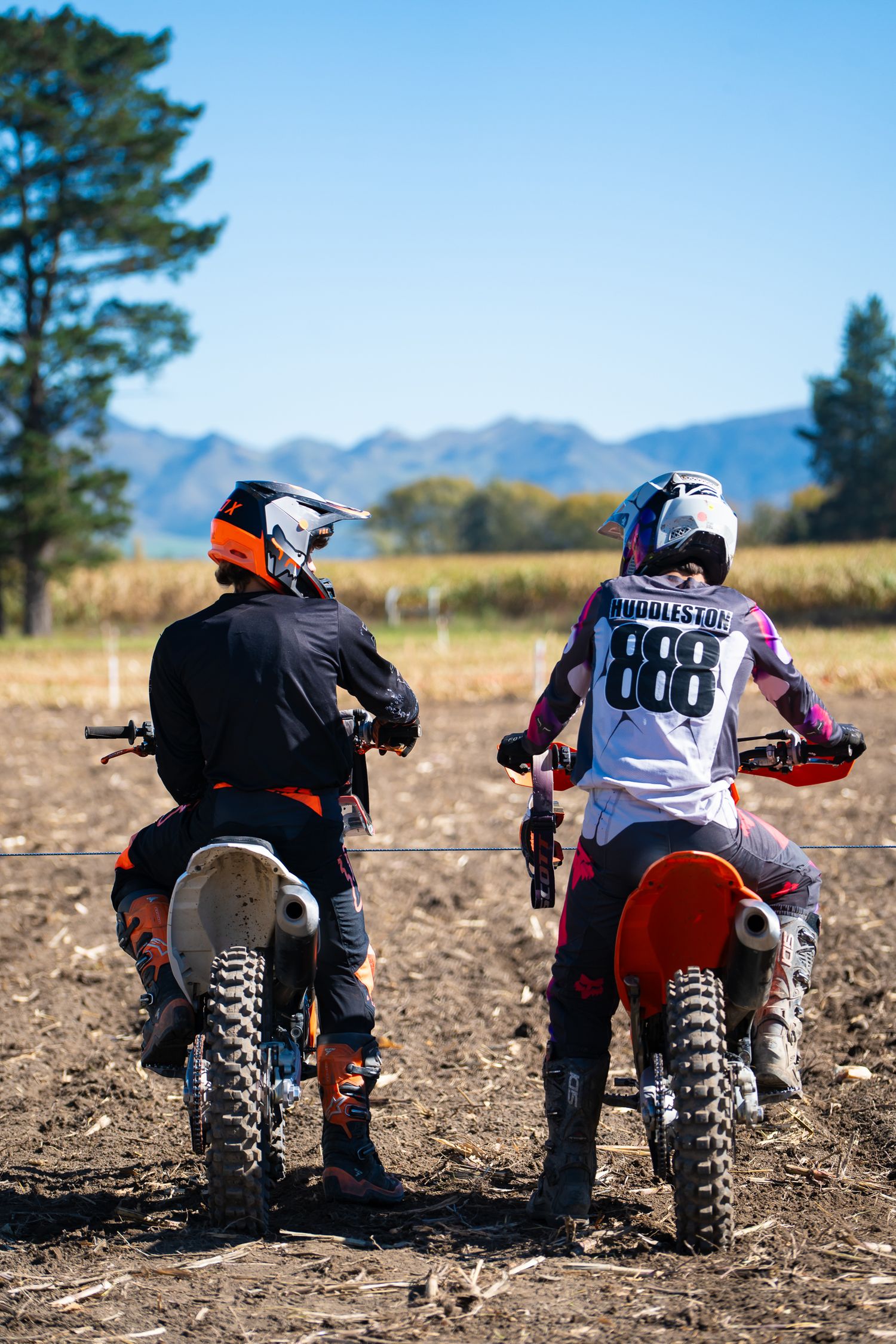 Motocross riders prepare their bikes at the starting line on a dirt track with mountains visible in North Canterbury.