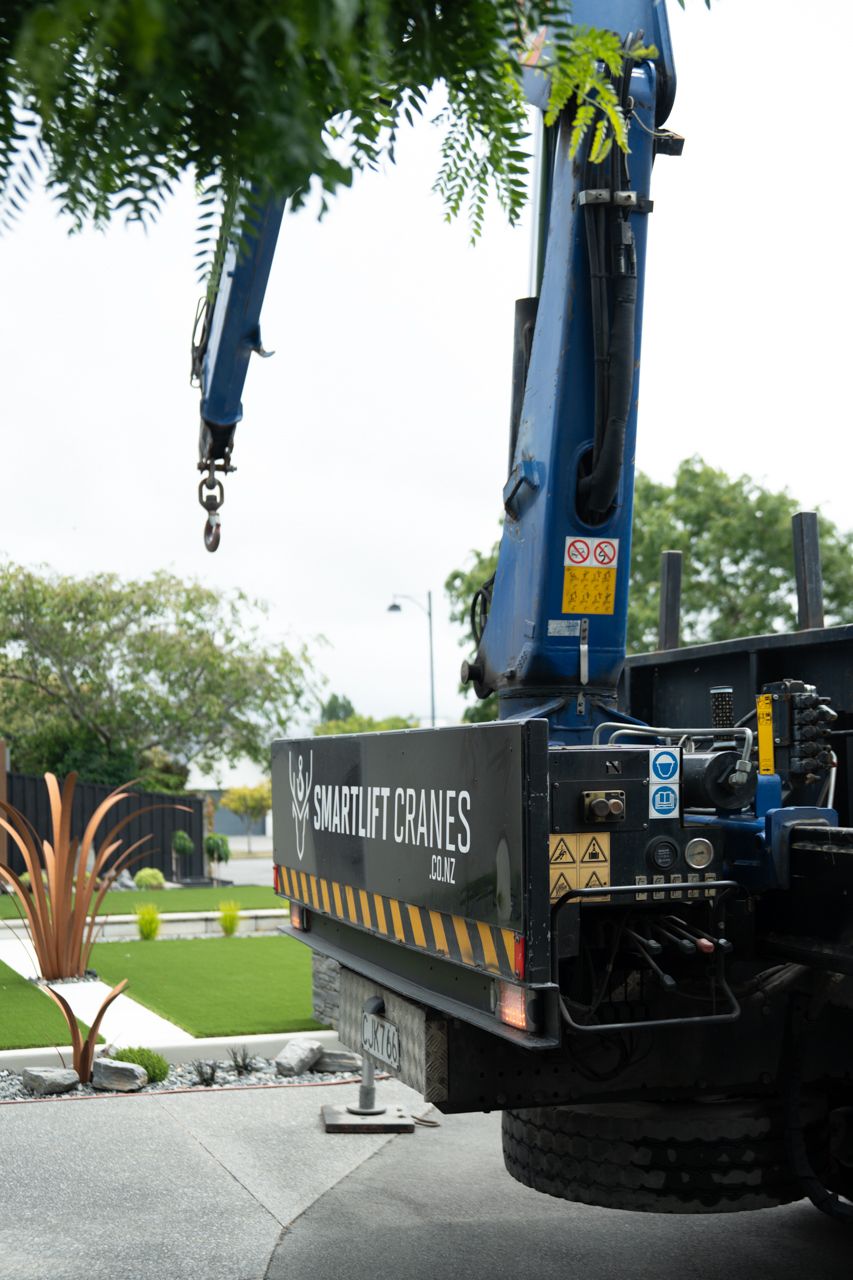 Smartlift Cranes truck with blue hydraulic crane arm extended, parked in a landscaped driveway in New Zealand.