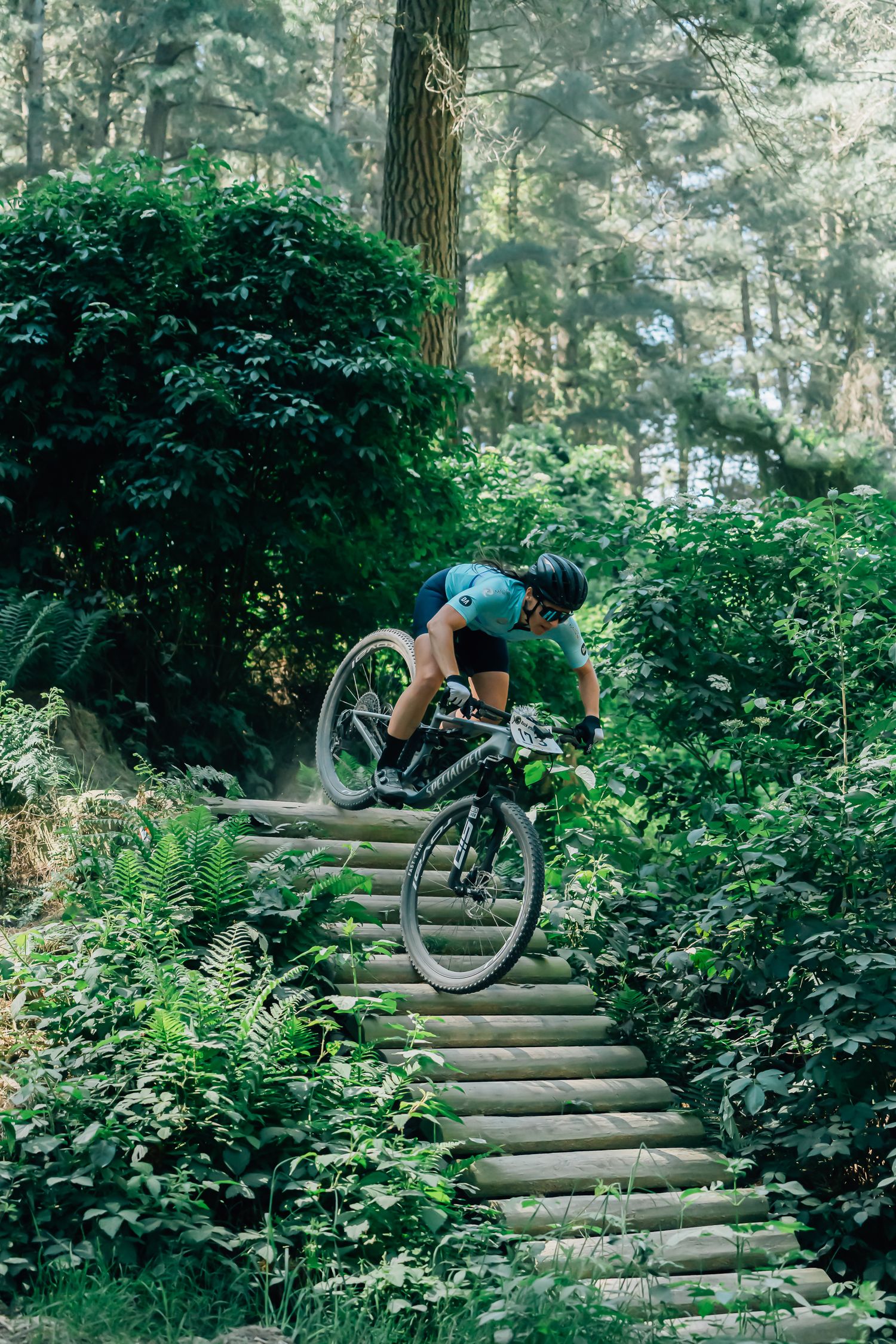 Mountain biker performs technical descent on wooden steps through lush green forest trail at the Crocodile Mountain Bike Park in Halswell.