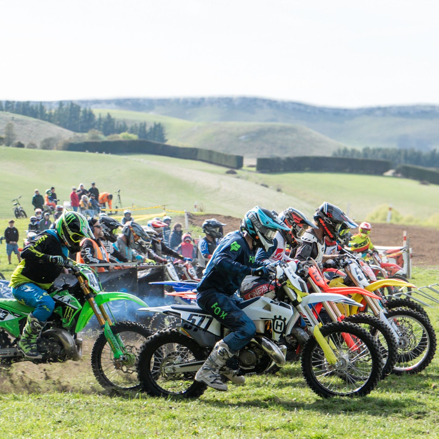 A group of motocross riders rolling off the start line on green grass with rolling hills in the background in North Canterbury.
