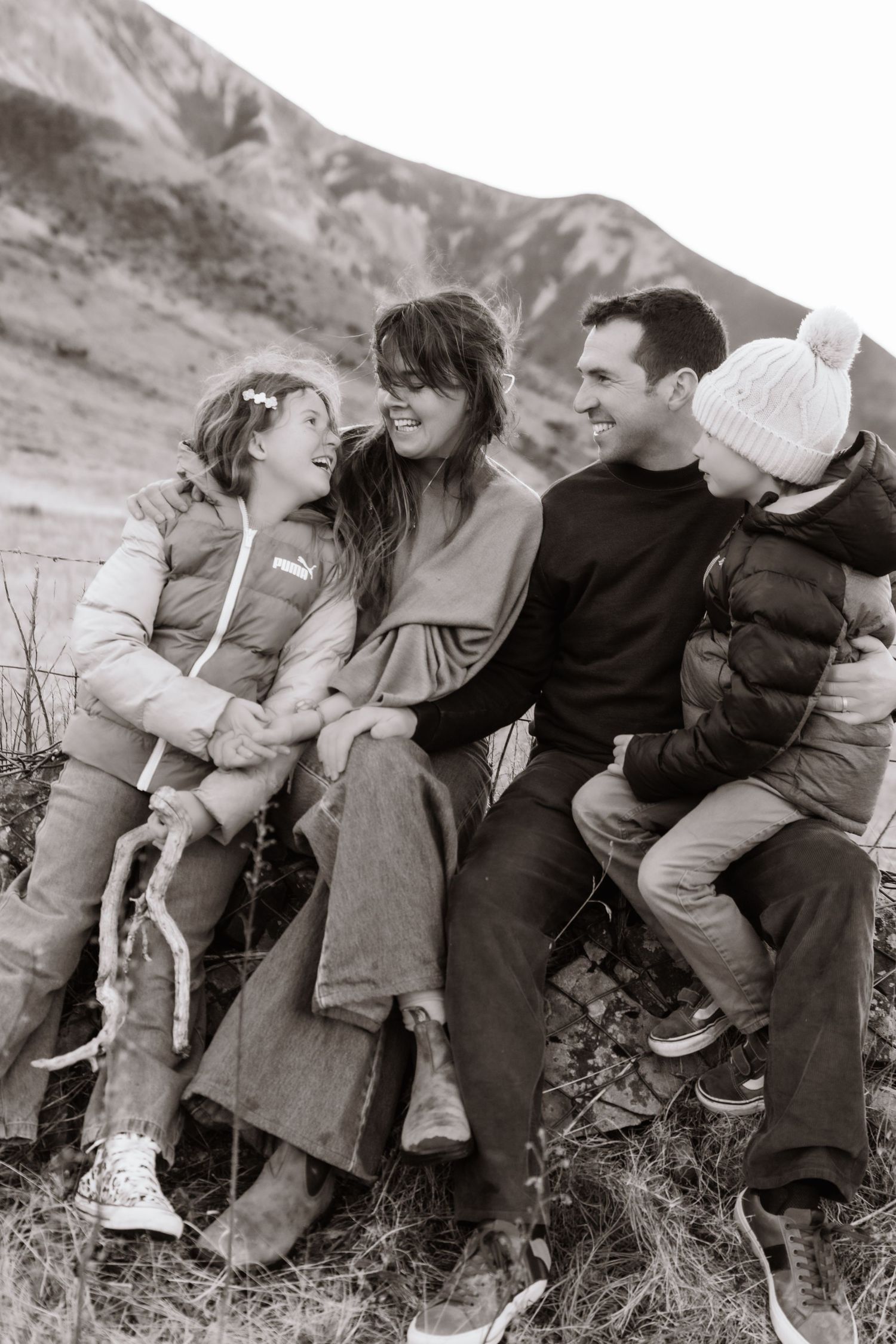 Black and white photo of a happy family of four laughing together outdoors near a mountain.