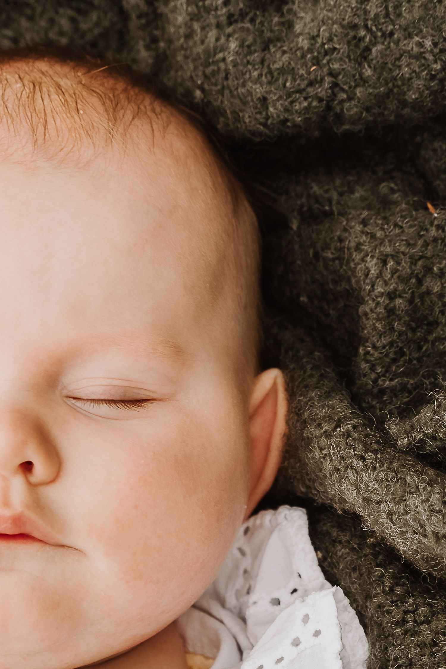 Peaceful sleeping newborn baby with red hair resting on a soft gray knit blanket.