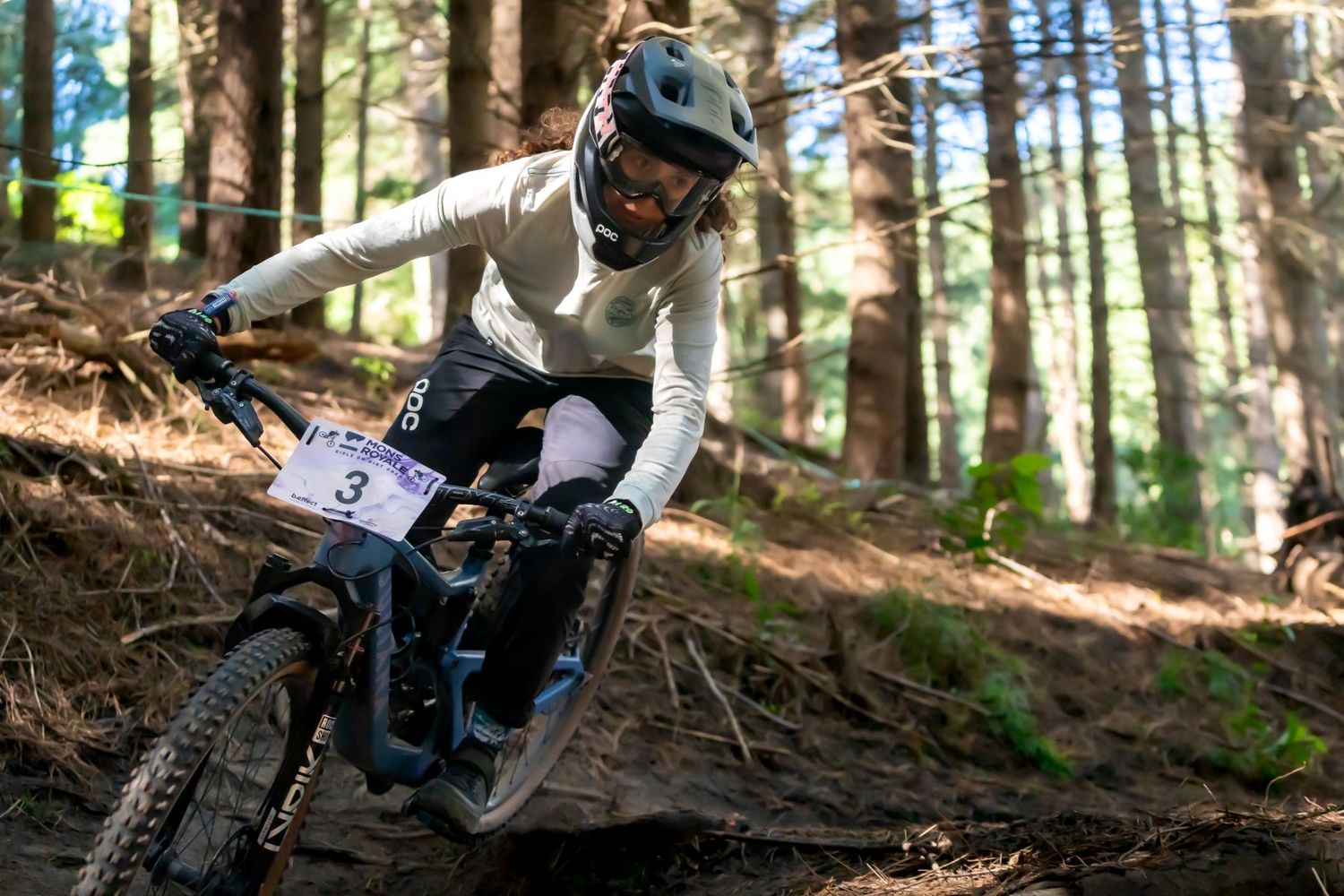 Mountain biker rides through a forest trail, navigating between trees in bright sunlight.
