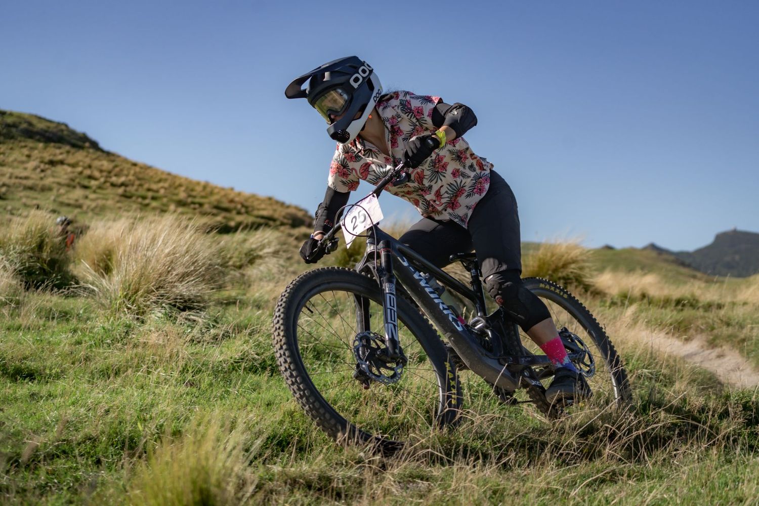 Mountain biker rides downhill on grassy terrain wearing protective gear and helmet during an outdoor adventure.