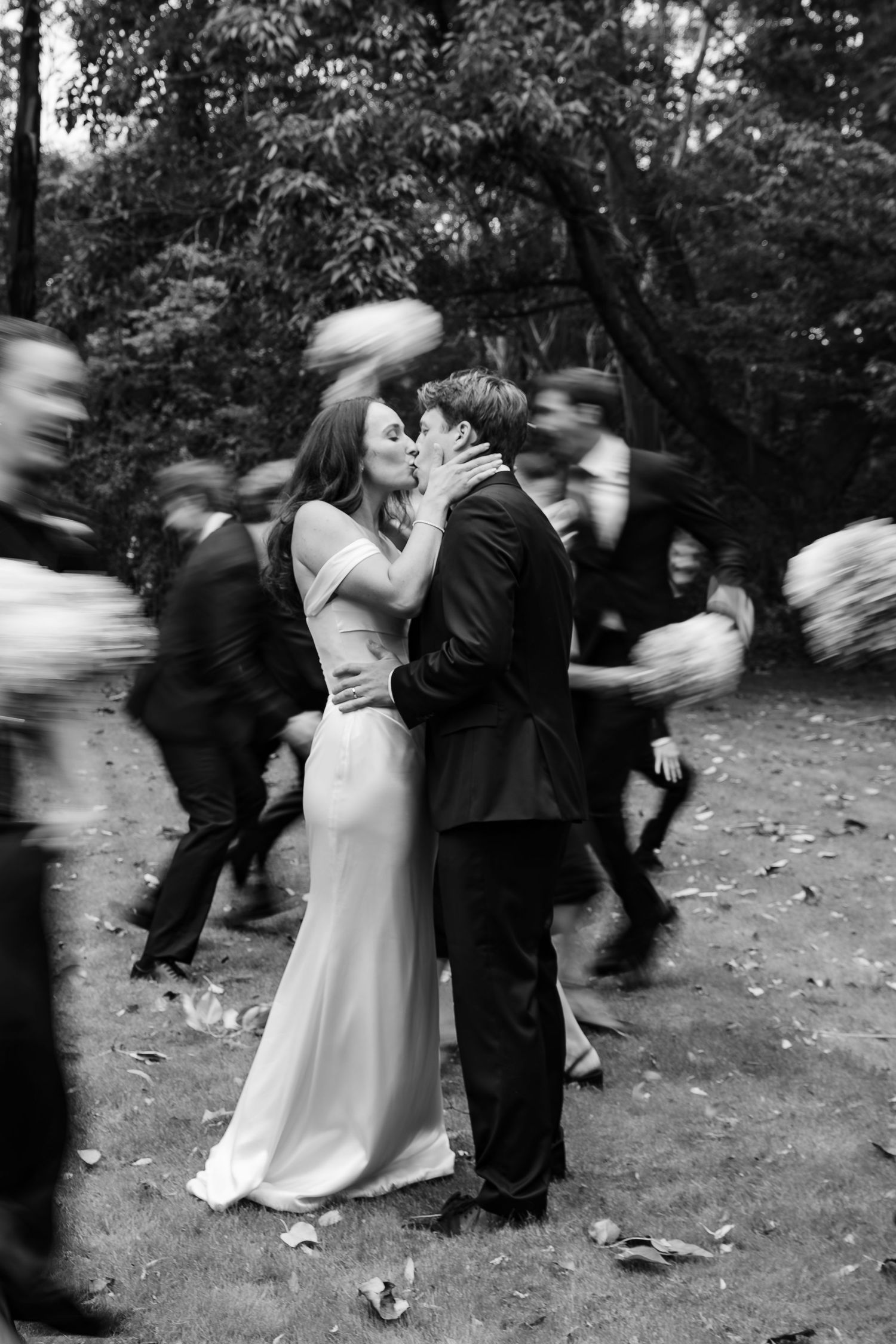 Black and white photo of bride and groom kissing while wedding guests move around them in a blur.