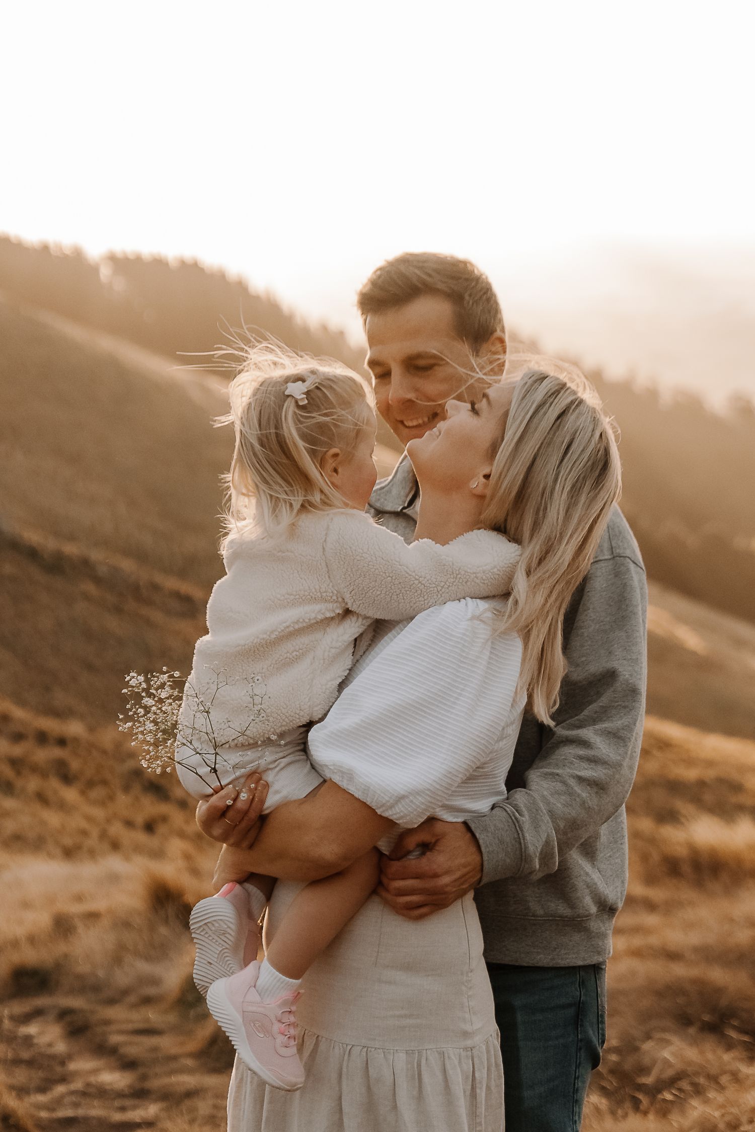 A happy family with a young girl holding wildflowers share a tender moment outdoors at golden hour.